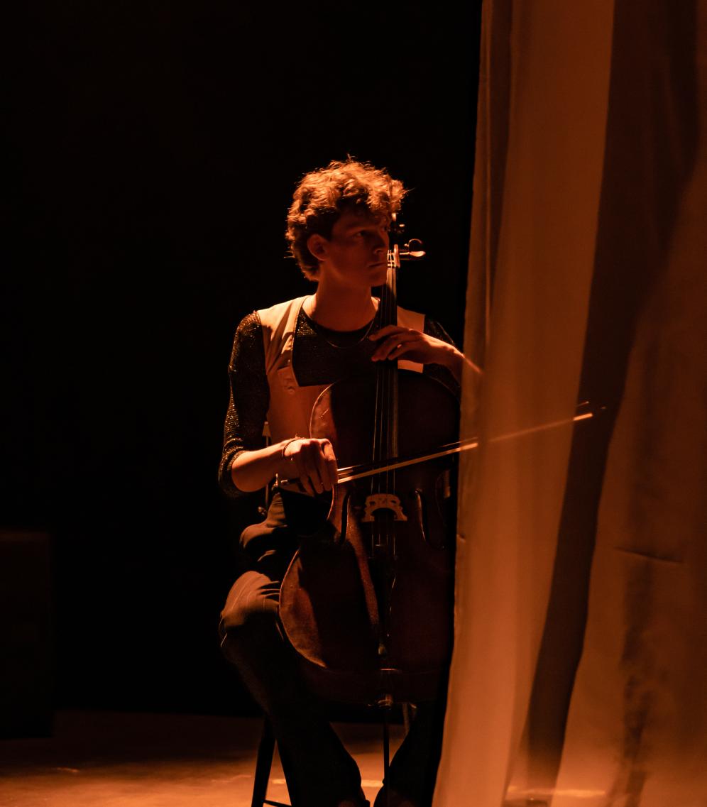 Cellist auf Theaterbühne, Blick nach rechts, transparenter Vorhang auf der rechten Seite 