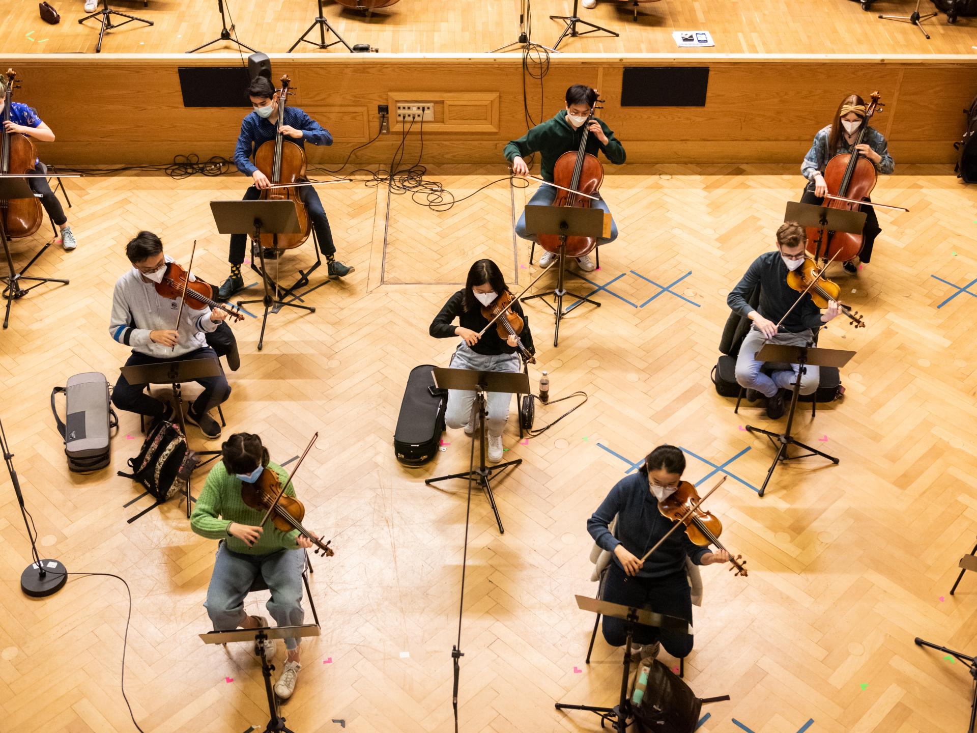 Mehrere Studierende mit Streichinstrumenten und Abstand im Orchester von oben fotografiert