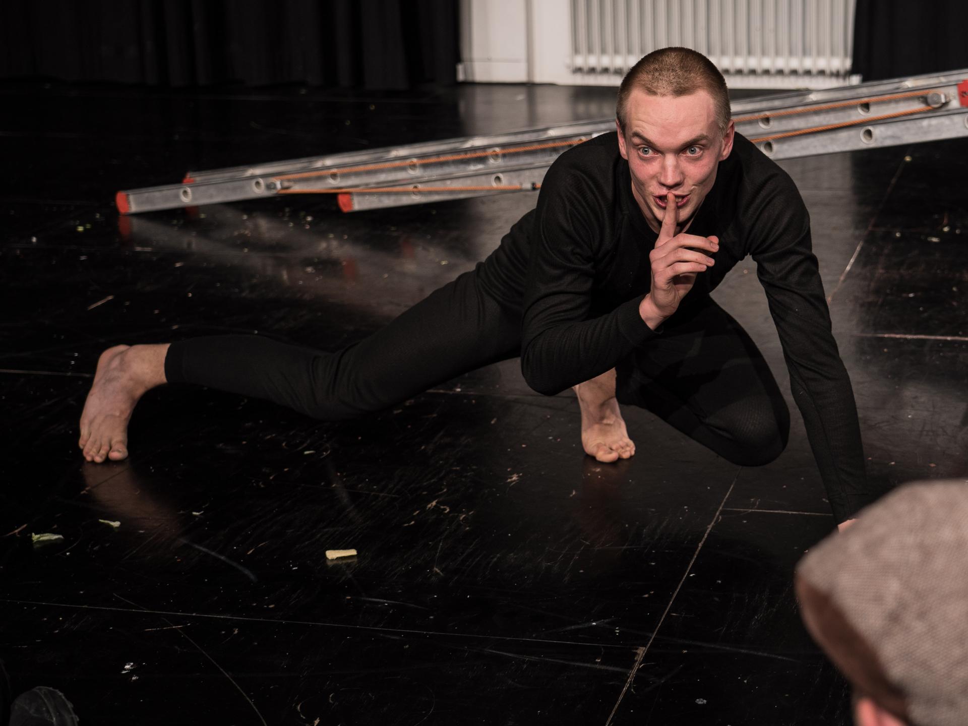 Max Böttcher wie ein Chamäleon auf dem Boden hockend, dem Publikum bedeutend leise zu sein. 