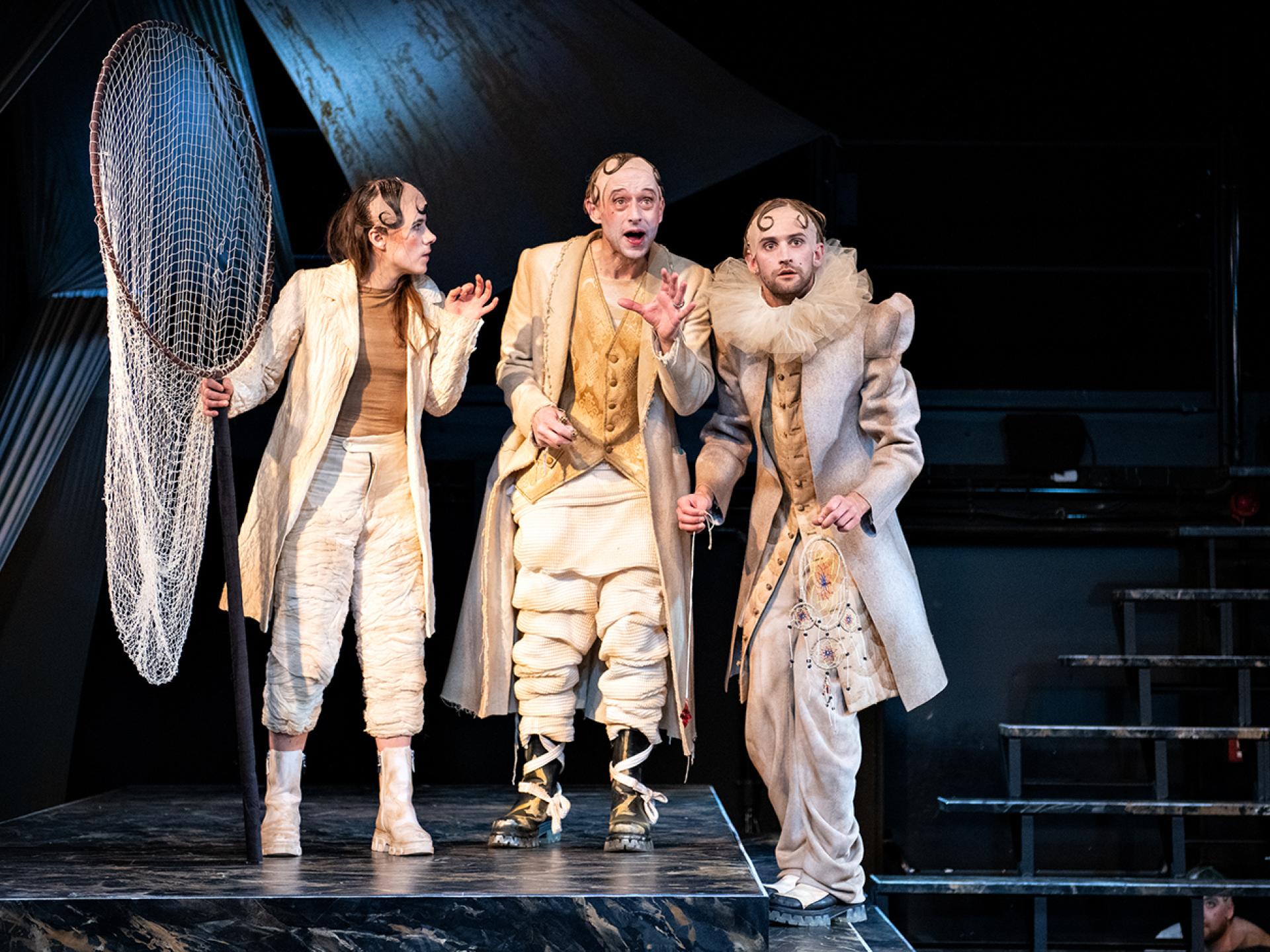 Olearius (gespielt von Esra Schreier) mit einem großen Köcher steht auf der Bühne mit den Figuren Kircher und Quast in der Inszenierung von "Tyll" am Theater Heidelberg im Dezember 2021.