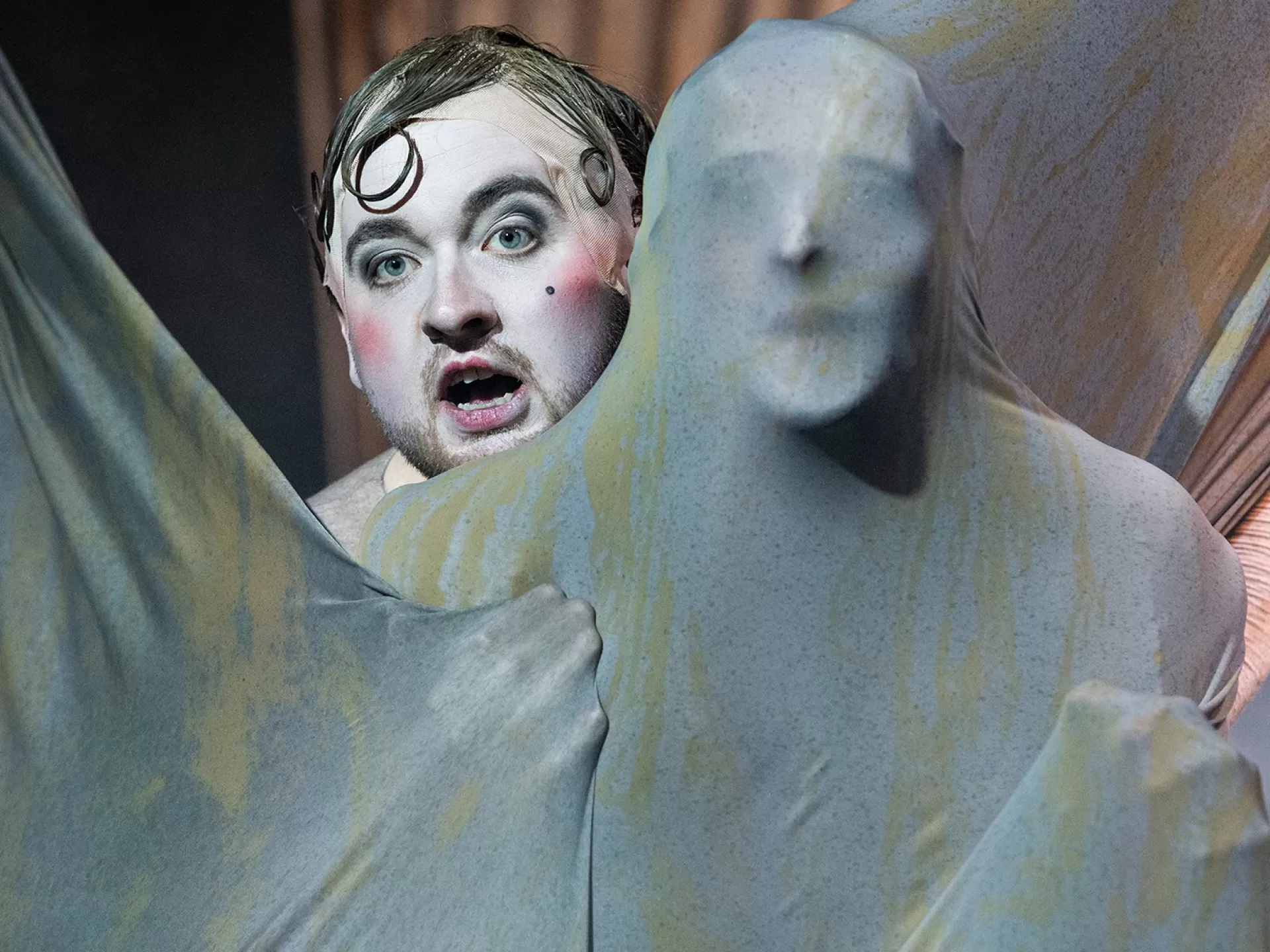 Die Figur Tyll (gespielt von Daniel Friedl) mit Kircher, der komplett in ein großes Stofftuch gehüllt ist, in der Inszenierung von "Tyll" am Theater Heidelberg im Dezember 2021.