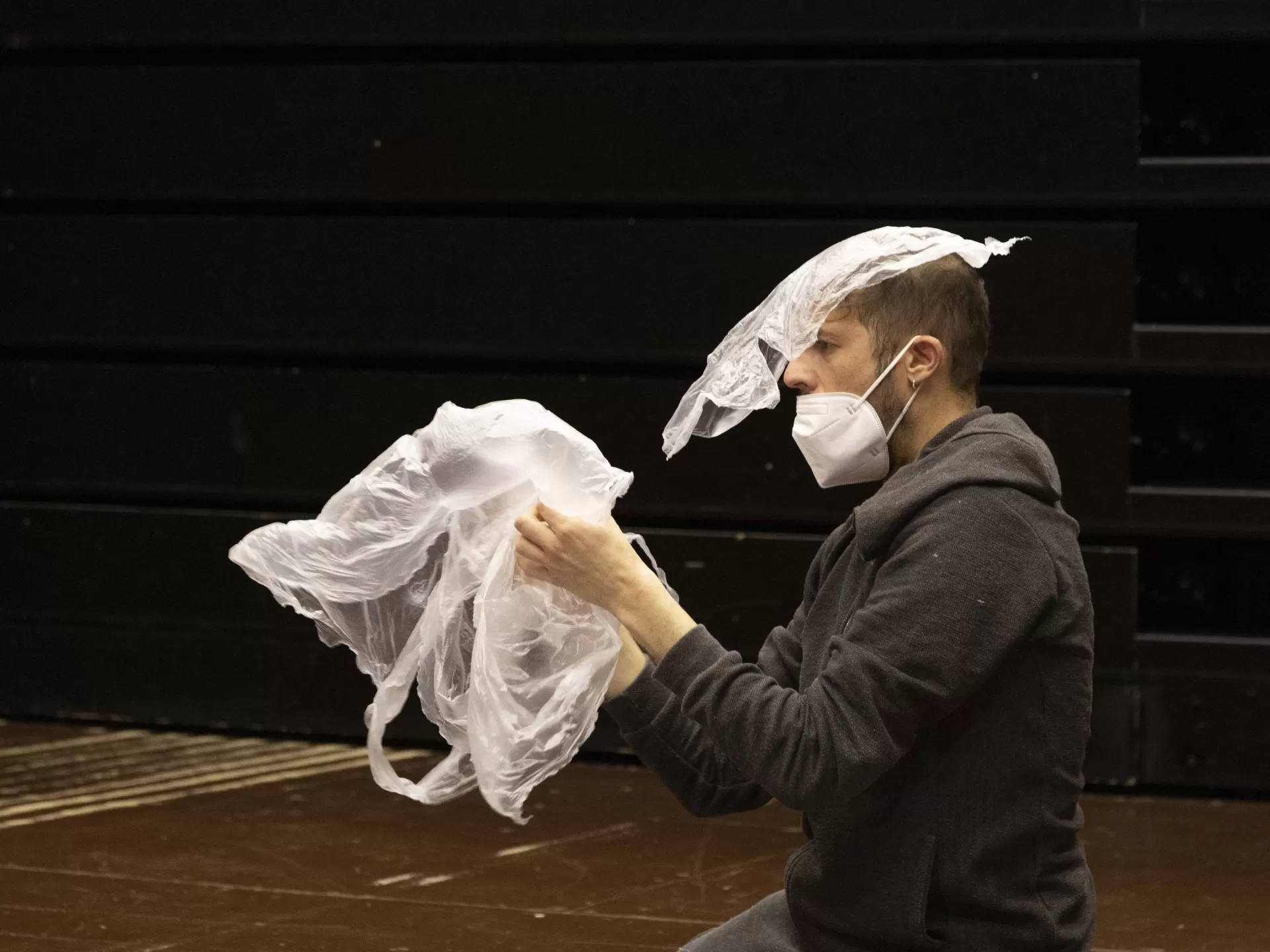 Ein Darsteller kniet auf der Bühne, eine Plastiktüte in den Händen und teilweise über dem Kopf.