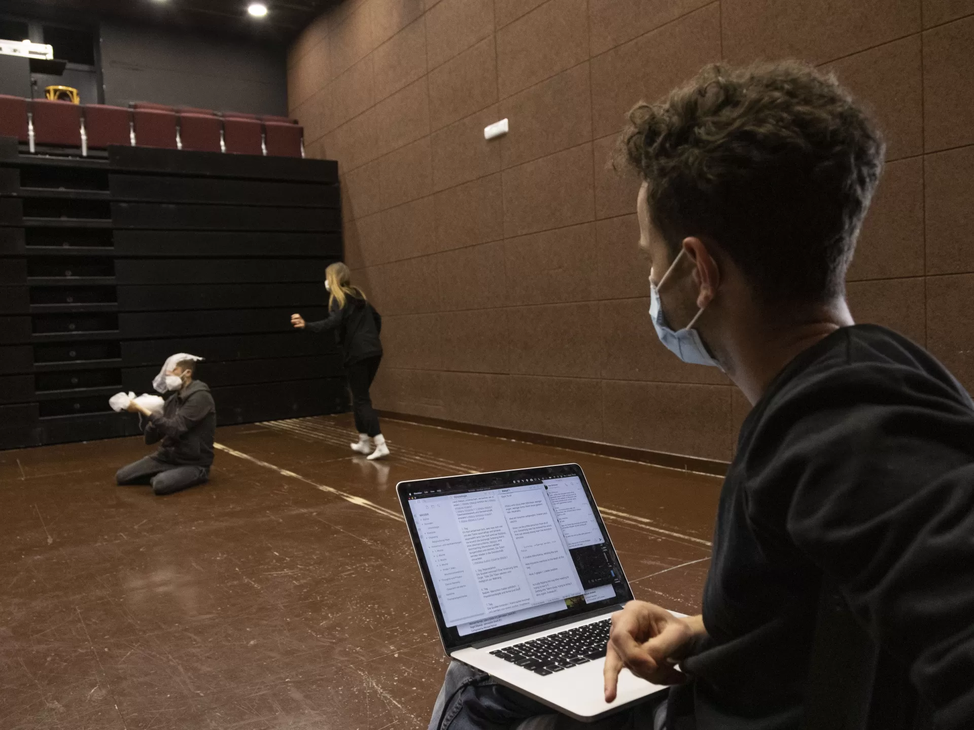 Regiestudent beobachtet die Probe für Agua, auf den Knien ein Laptop.