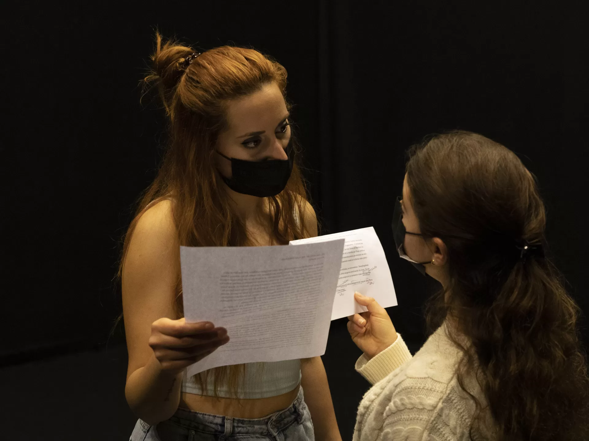 Zwei Studentinnen blicken sich an, halten Textblätter in der Hand