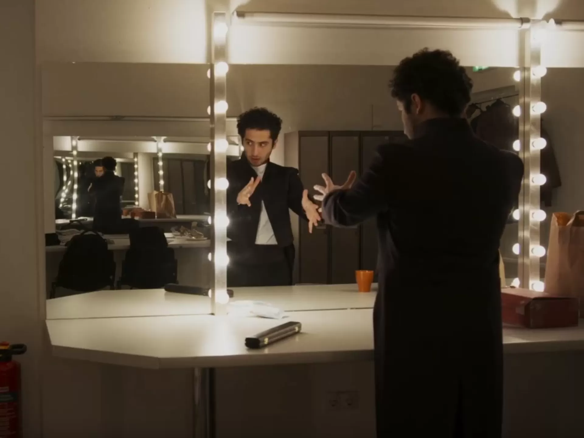 Ein Dirigent steht nervös und mit ausgestreckten Armen vor dem Spiegel in seiner Garderobe.