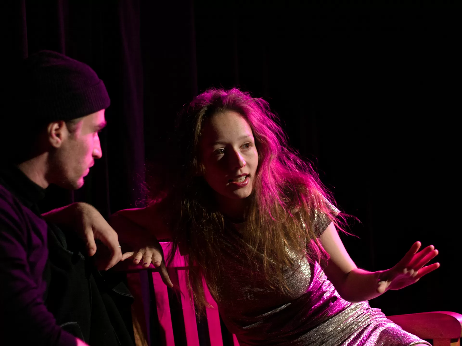 Ein Mann und eine Frau sitzen auf einer Bank, die Frau hat lange Haare, spricht und gestikuliert mit einer Hand.