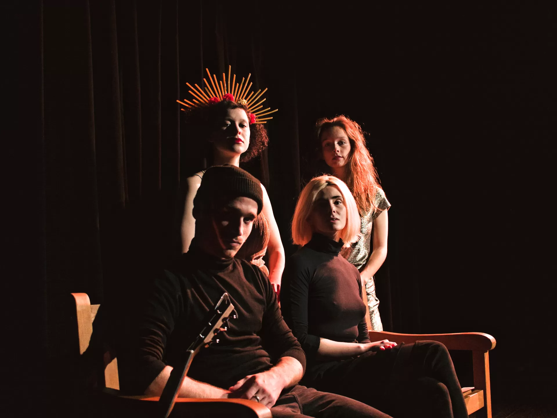 Die Schauspieler*innen und die Regisseurin sitzen auf einer Bank und schauen in die Kamera (Arbeitsfoto).