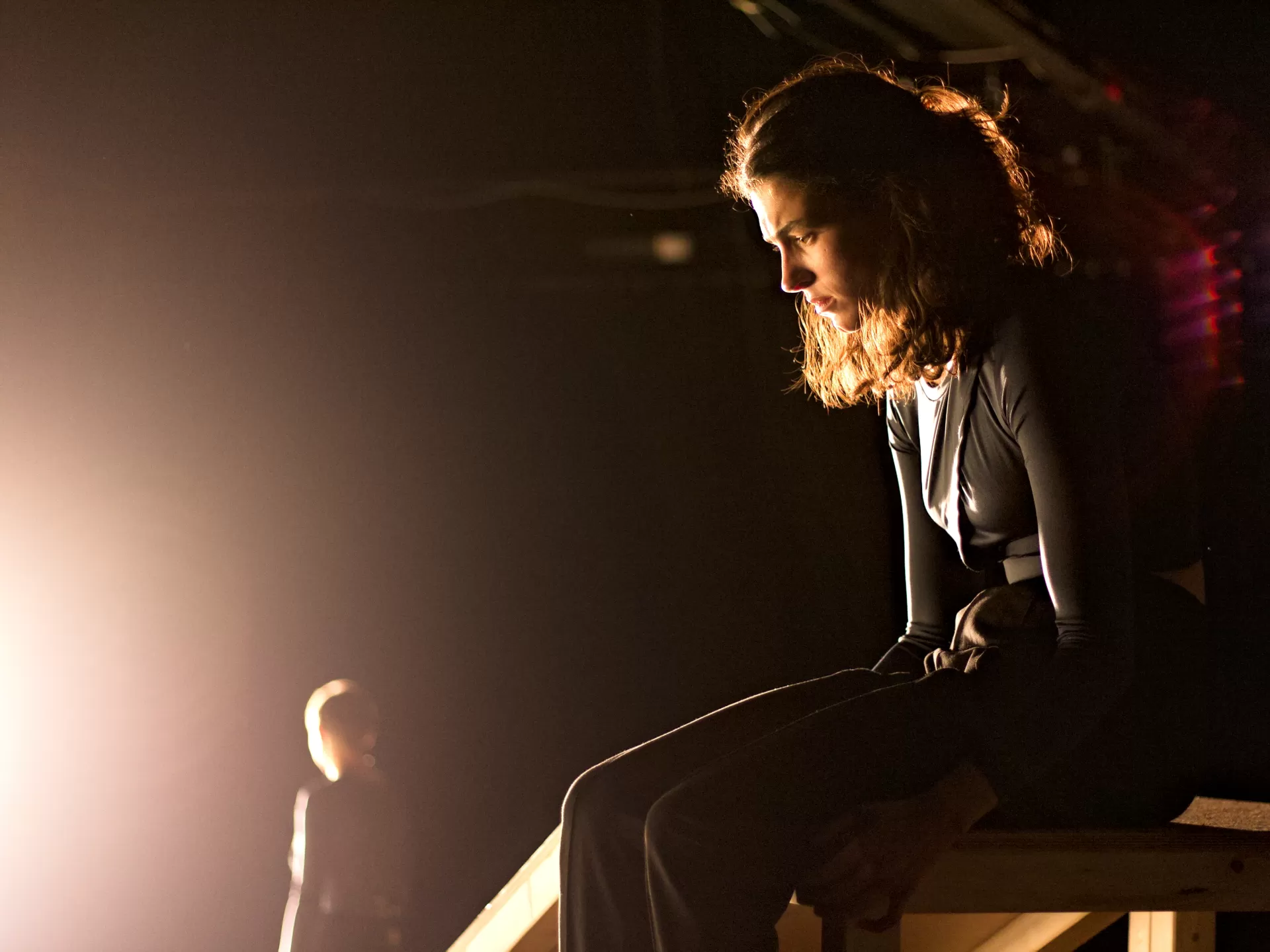 Eine Frau sitzt auf der Kante auf einem Holzpodest und schaut nachdenklich nach unten.