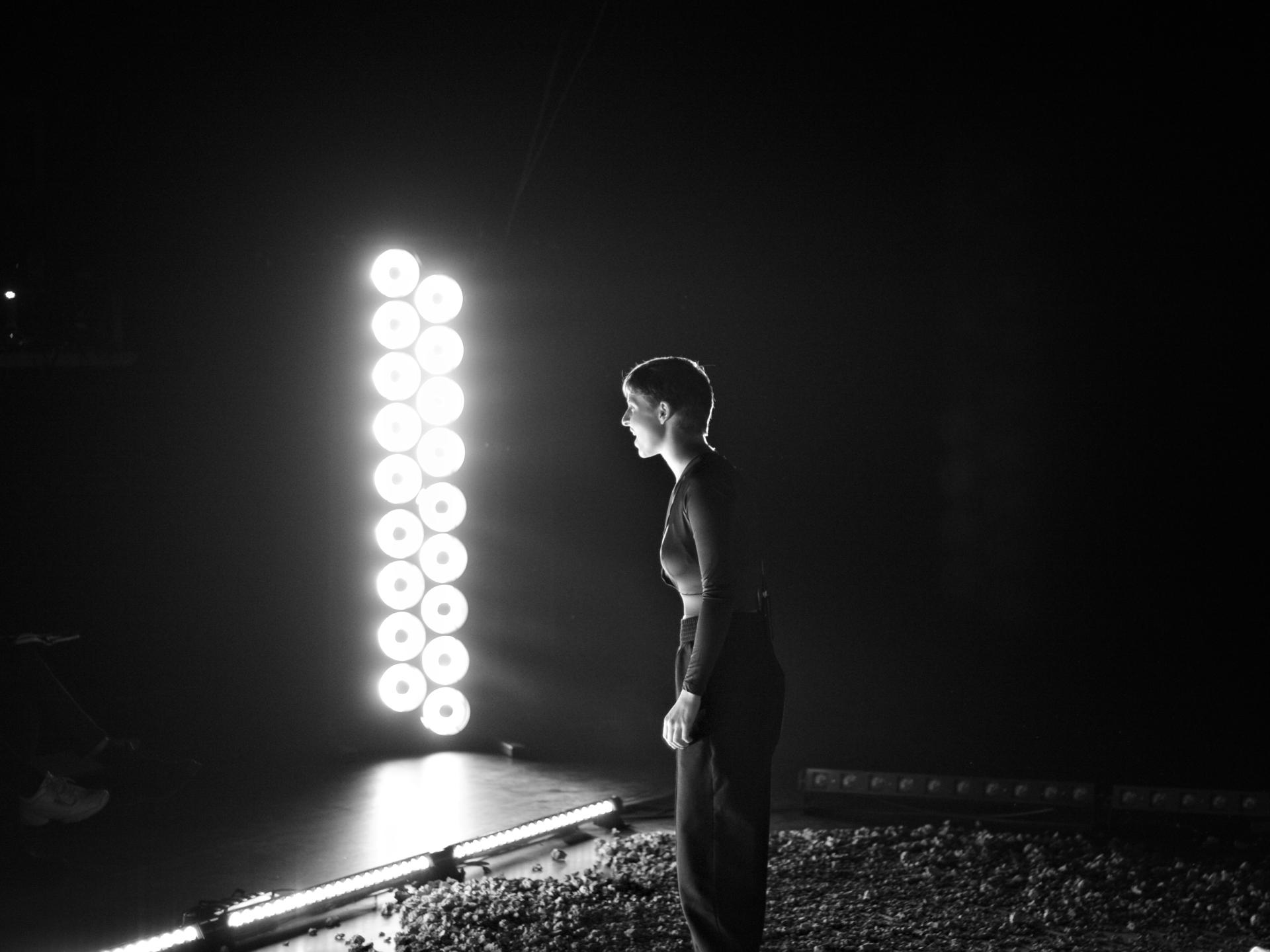 Eine Frau steht im Licht mehrerer Scheinwerfer und redet leidenschaftlich (Bild ist schwarz-weiss).
