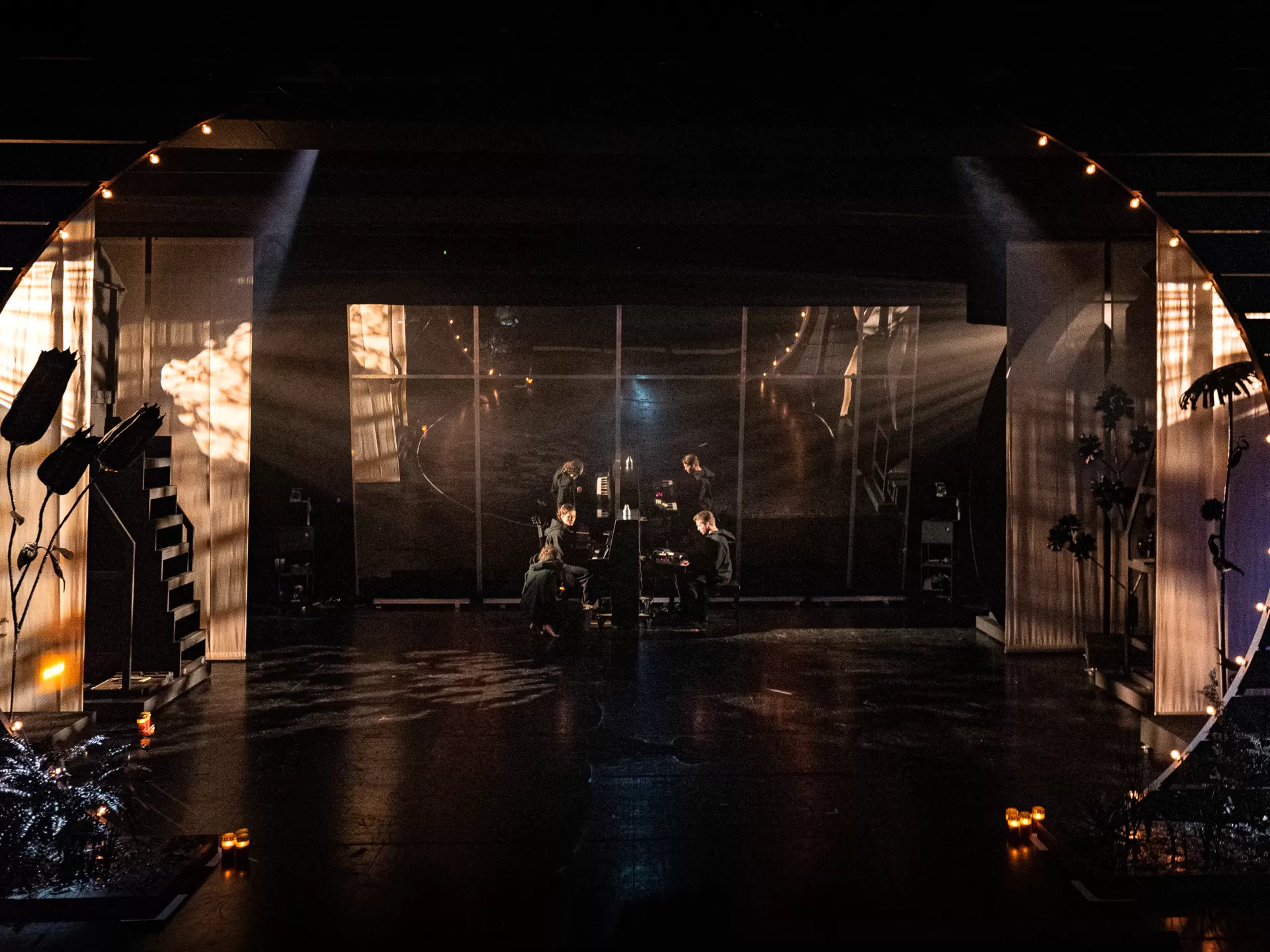 Frontalansicht auf die Bühne, die warm beleuchtet ist und der Schauspielende am Klavier musizieren.