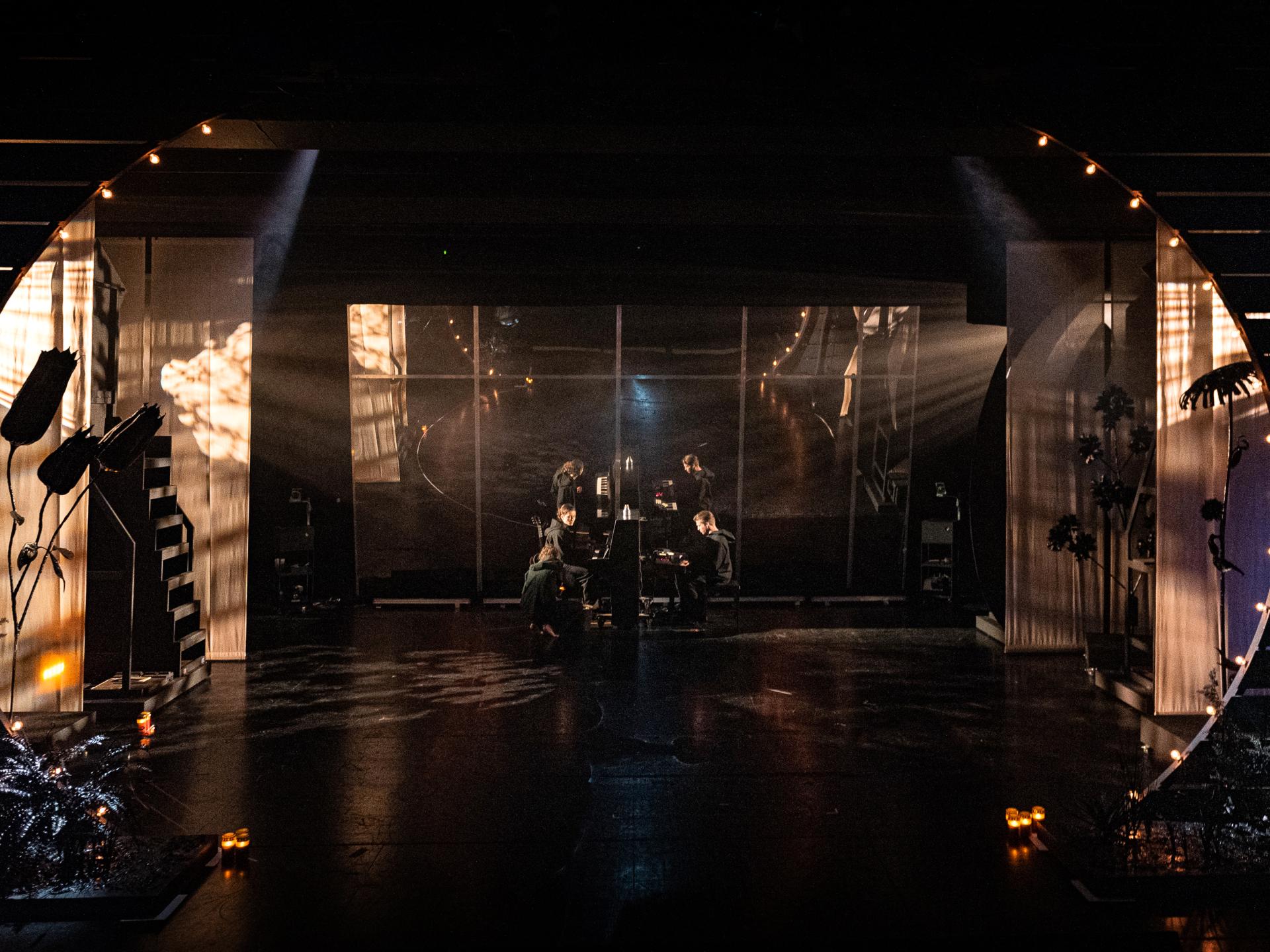 Frontalansicht auf die Bühne, die warm beleuchtet ist und der Schauspielende am Klavier musizieren.