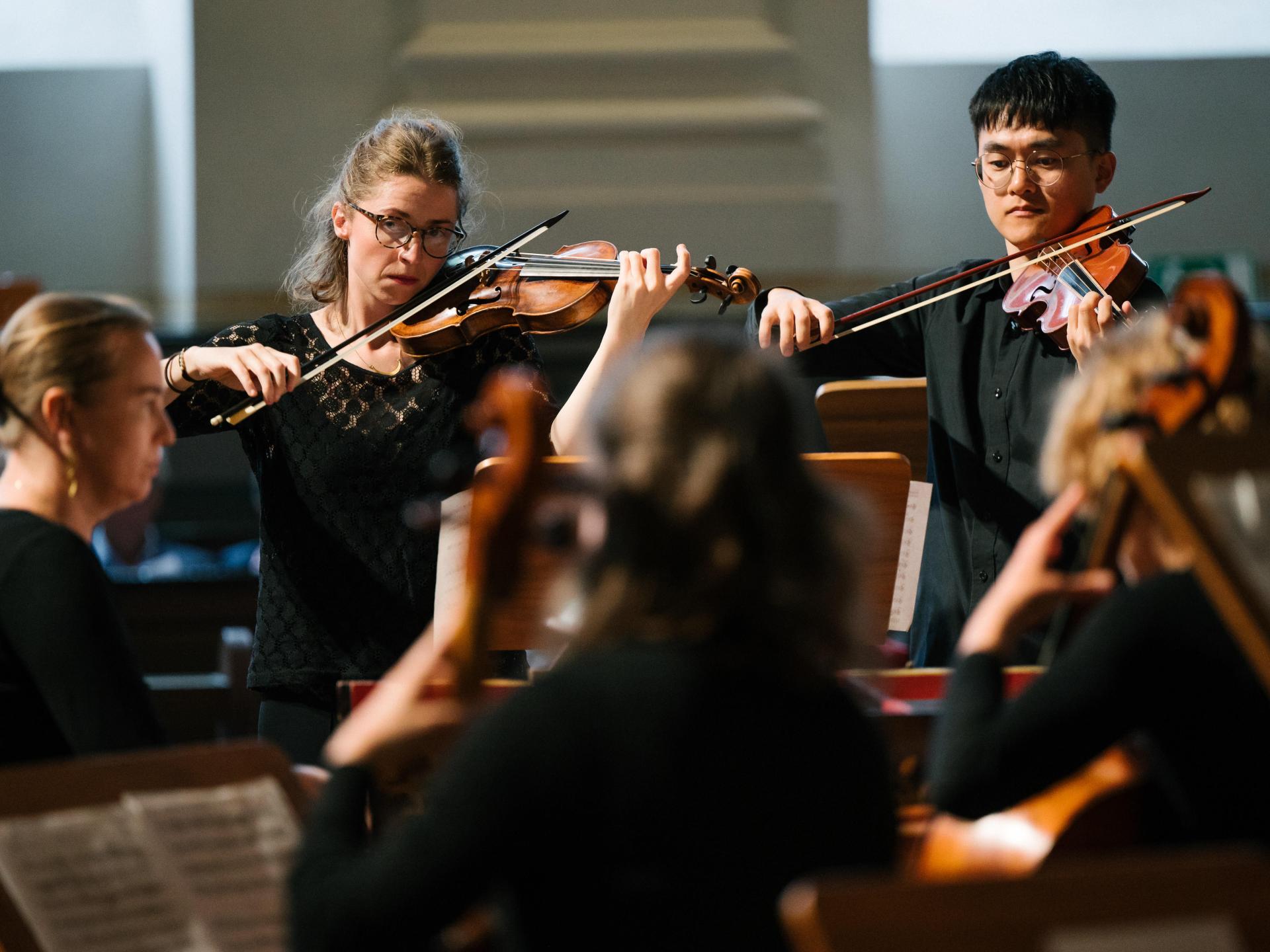 Zwei Streicher in einem Orchester, das mit historischen Instrumenten besetzt ist.