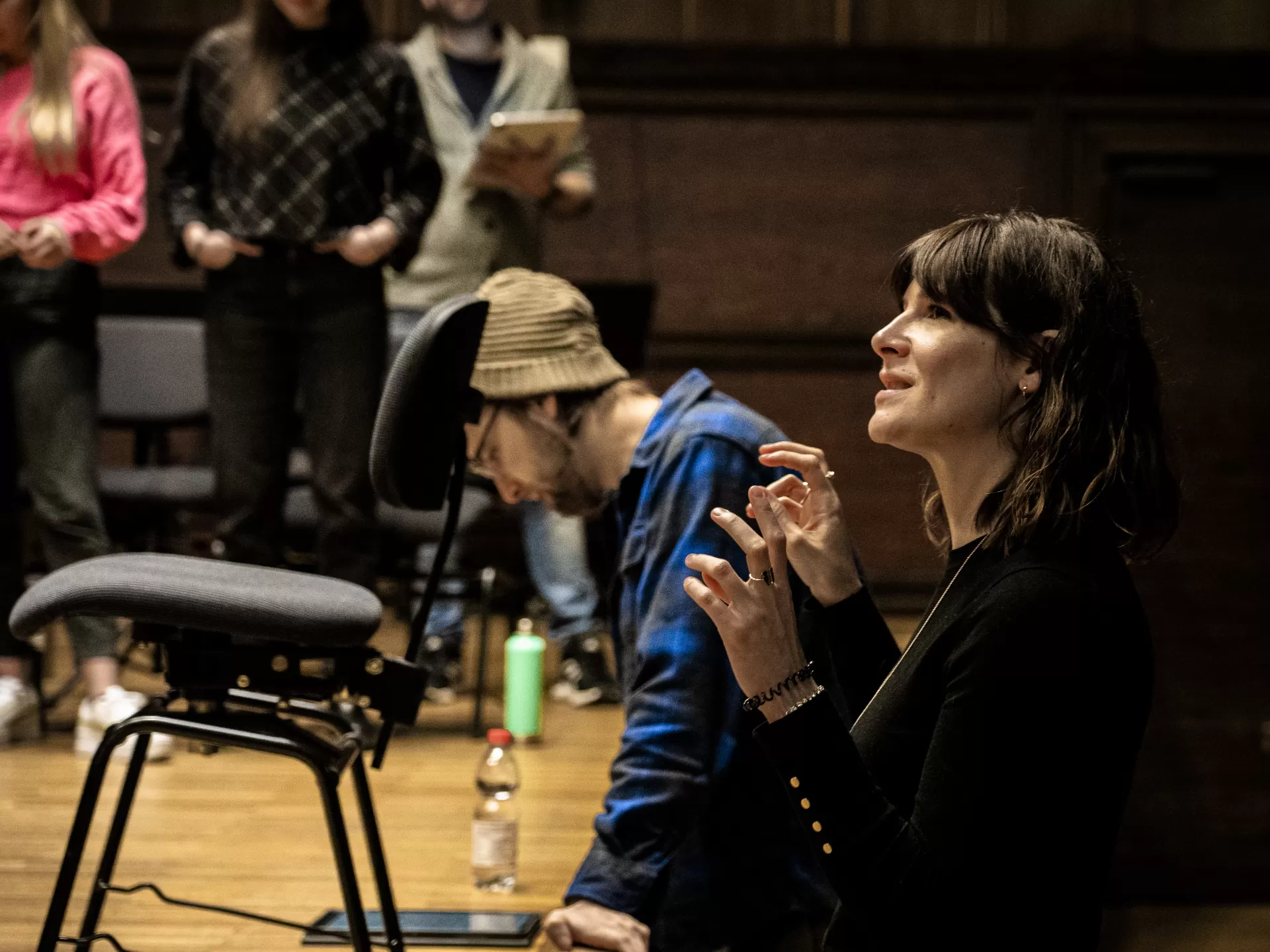 Eine Frau steht am Bühnenrand und blickt hoch zur Bühne, sie sagt etwas zu den Personenn auf der Bühne und gestikuliert dabei mit den Händen.