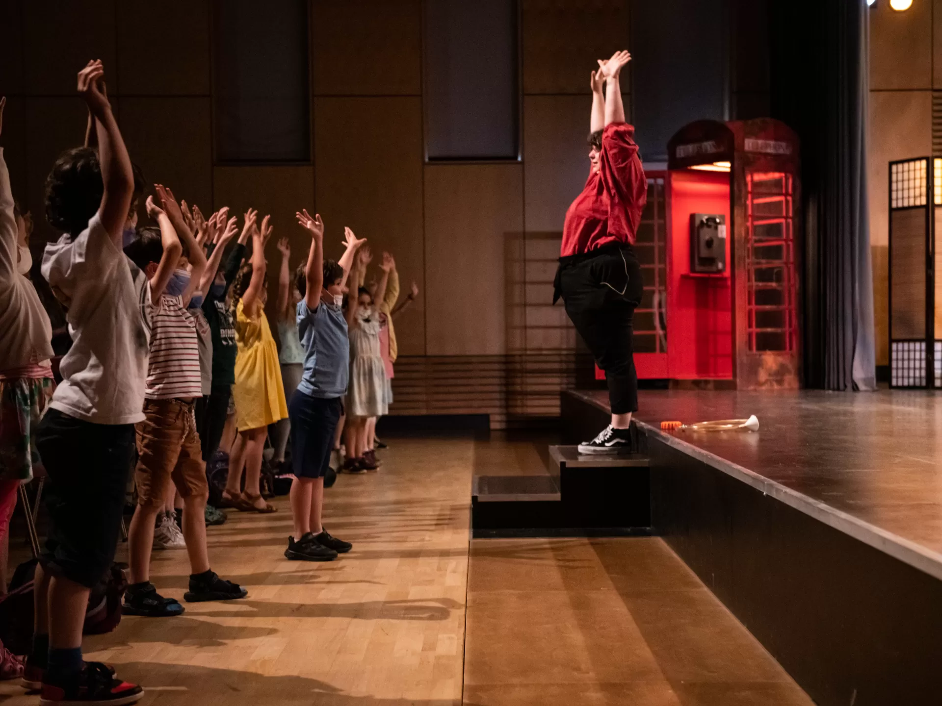 Mitmachkonzert für Kinder. Rechts auf der Bühne macht eine Musikerin vor, wie die Kinder die Arme heben sollen. Links im Bild Kindergruppe, die mitmacht.