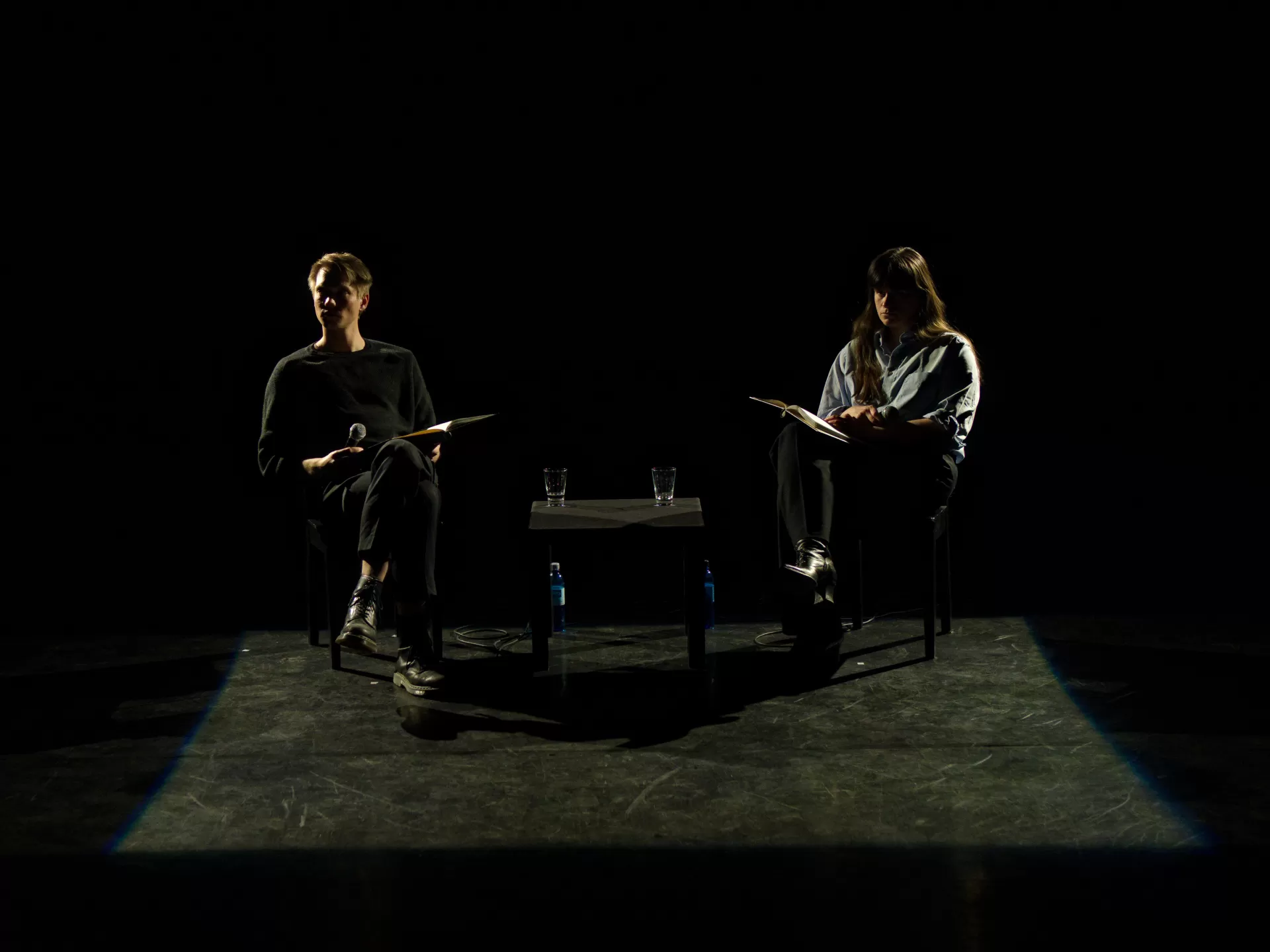 Ein Schauspieler und eine Schauspielerin sitzen im Halbschatten, ihr Gesichter sind nicht zu erkennen