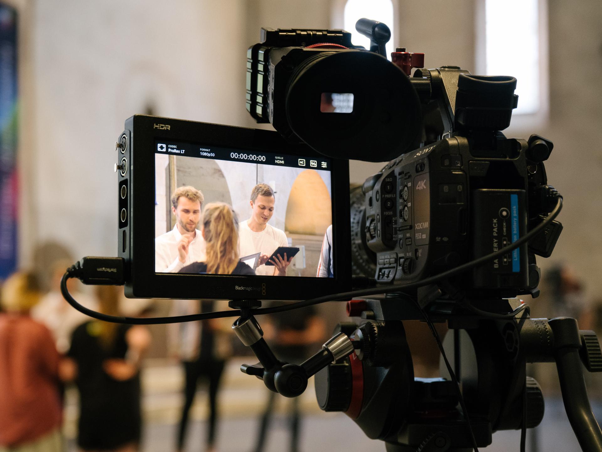 Blick auf das Display einer Videokamera, in der drei Sänger*innen auf der Bühne des Kloster Eberbach zu sehen sind.