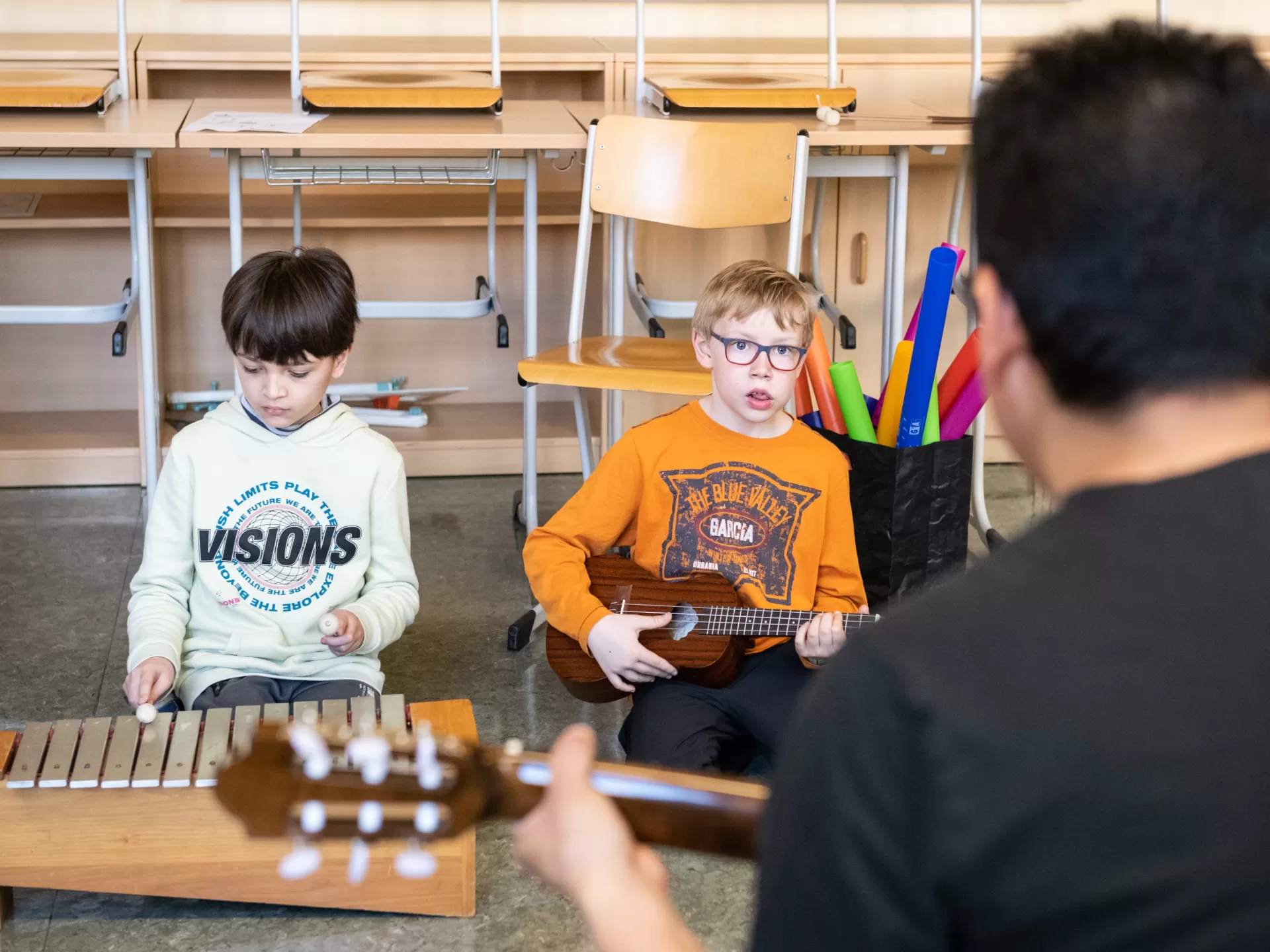 Zwei Kinder mit Musikinstrumenten, vor ihnen ein Student mit einer Gitarre.