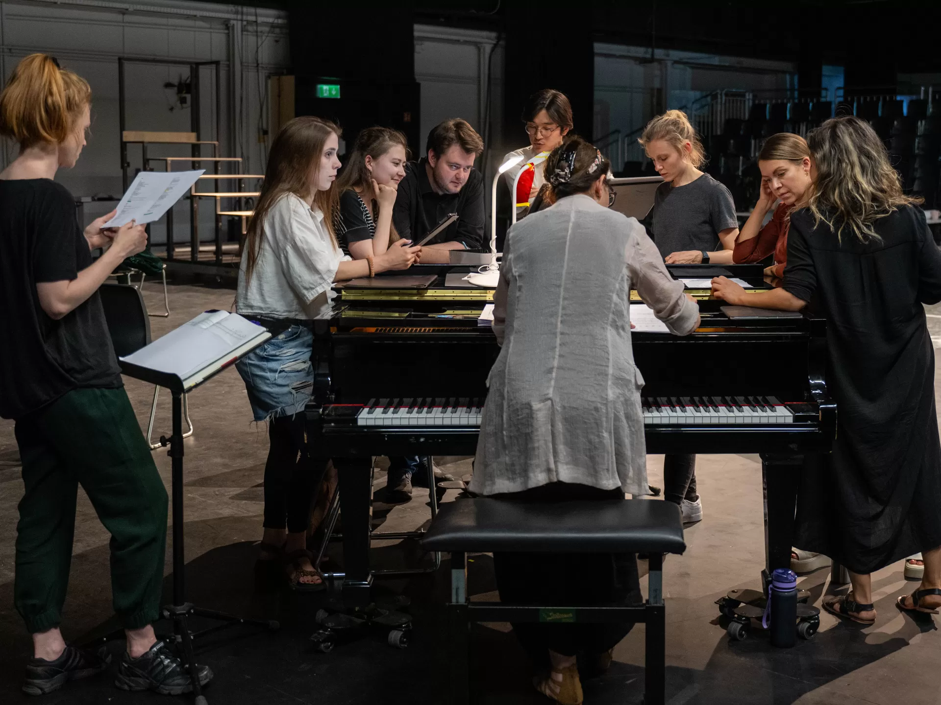 Gruppe von acht Sänger*innen steht während einer Probe um einen Flügel herum