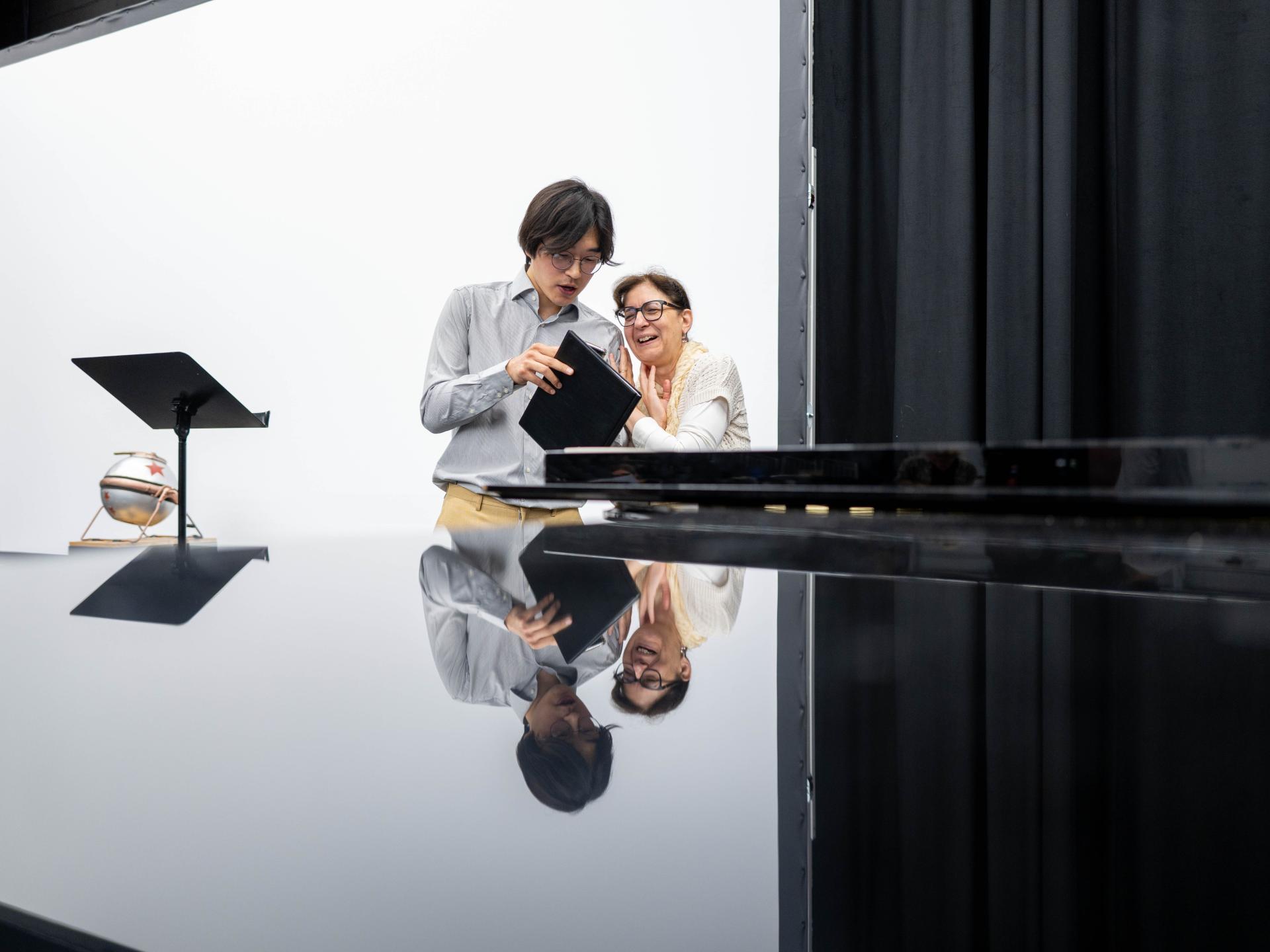 Sänger steht am Klavier und blickt mit Pianistin in die Noten