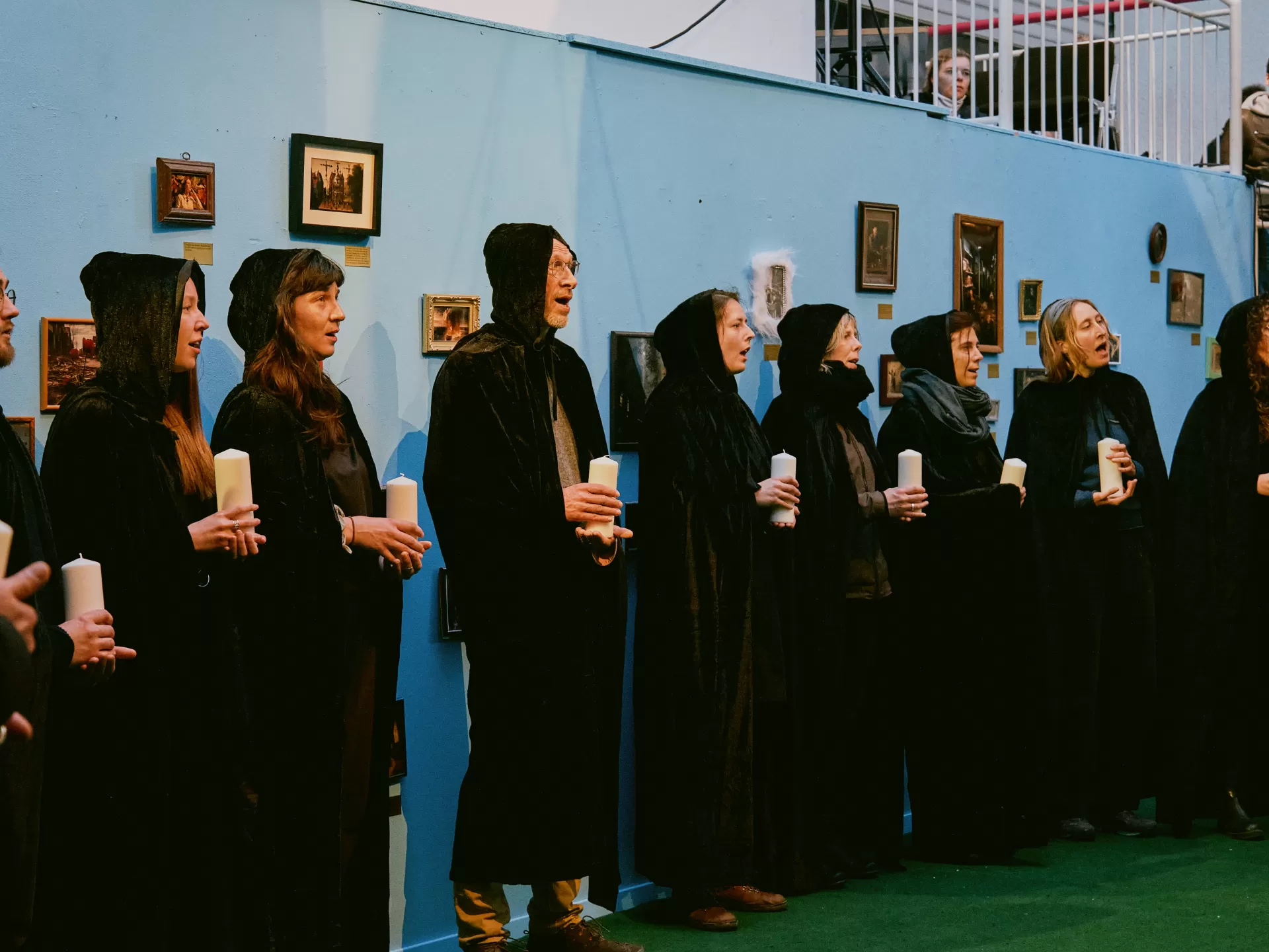 Personen in schwarzen Kutten singen mit Kerzen in der Hand.