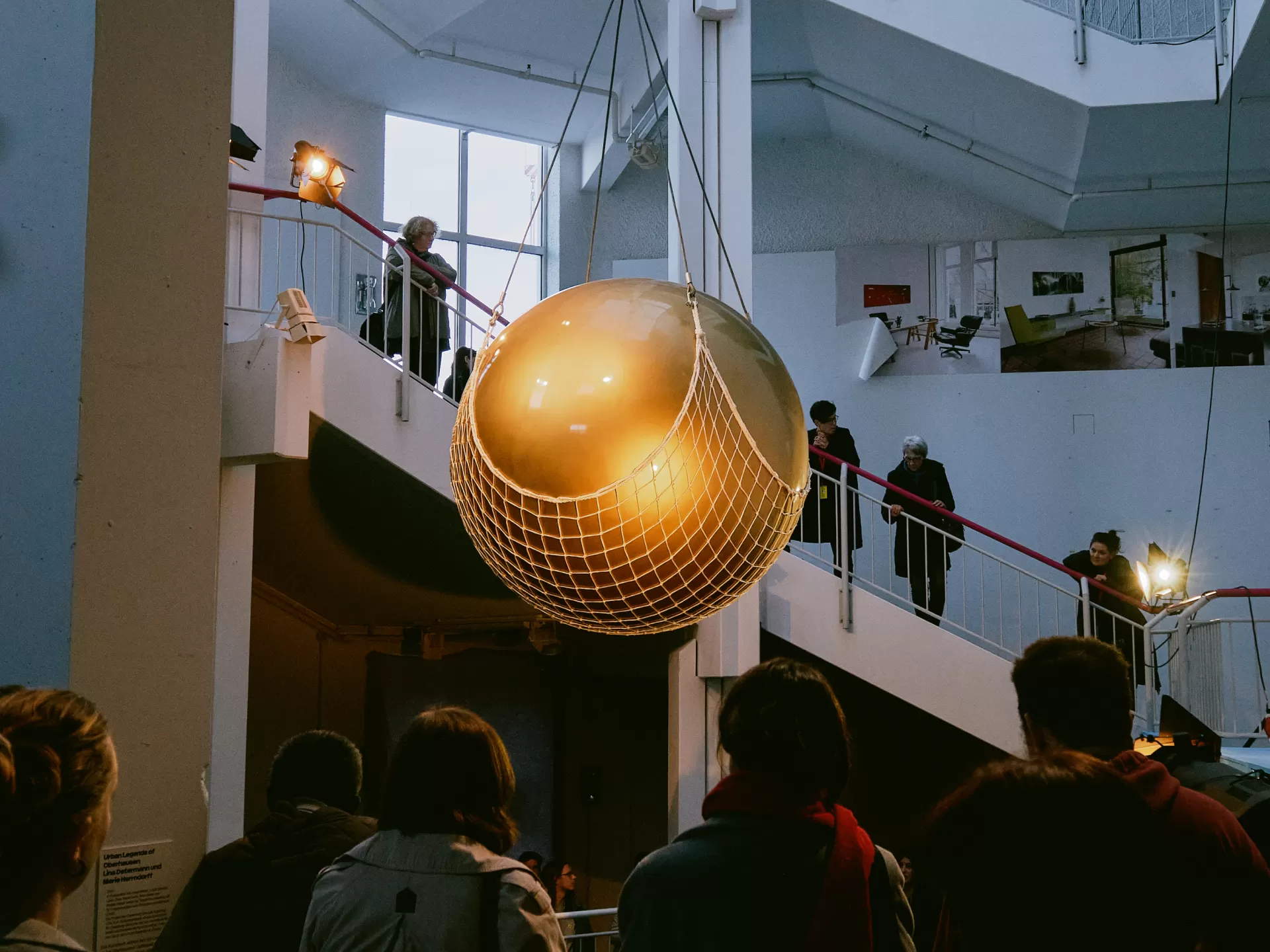 Die Goldene Kugel hängt über den in schwarzen Kutten gekleideten Mitwirkenden in einem weißen Treppenhaus.