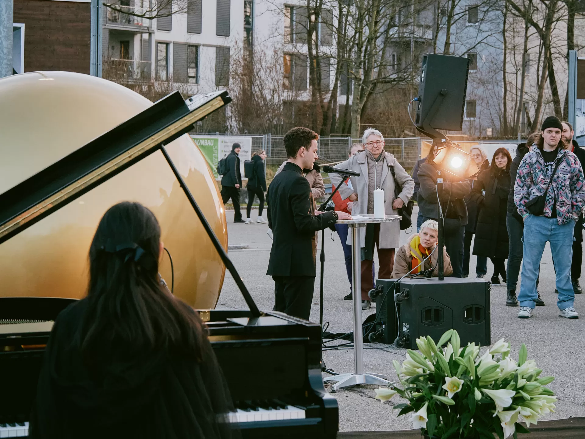 Ein junger Mann in schwarzem Anzug hält eine Rede. Davor sieht man die goldene Kugel und die Pianistin.