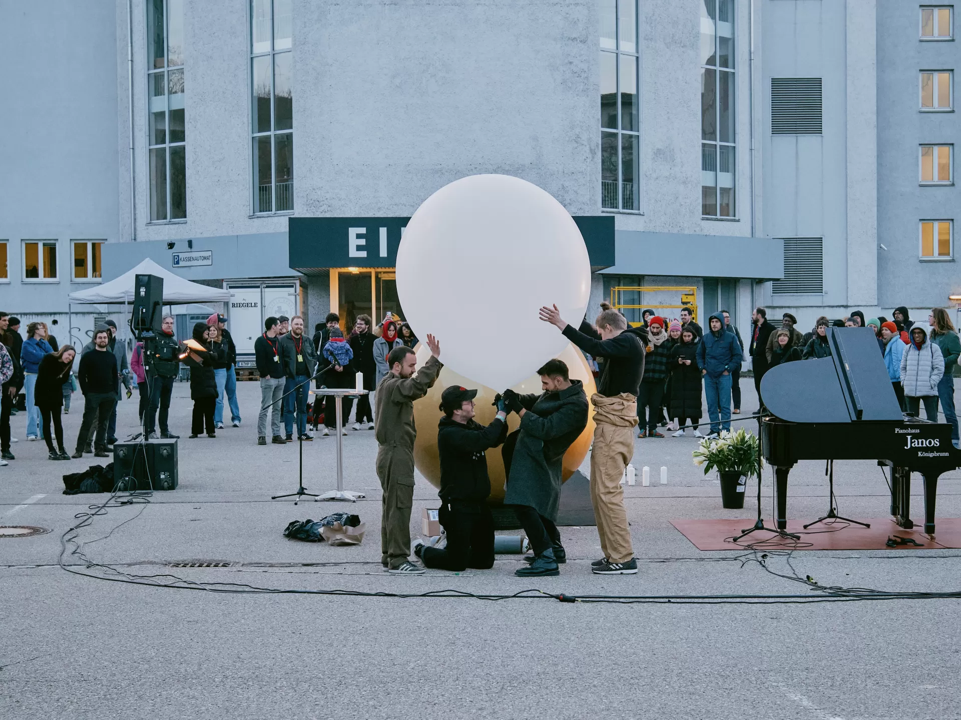 Vier Männer bereiten den Aufstieg des weißen Wetterballons vor. Sie stehen vom Publikum aus gesehen halb verborgen hinter der Goldenen Kugel.