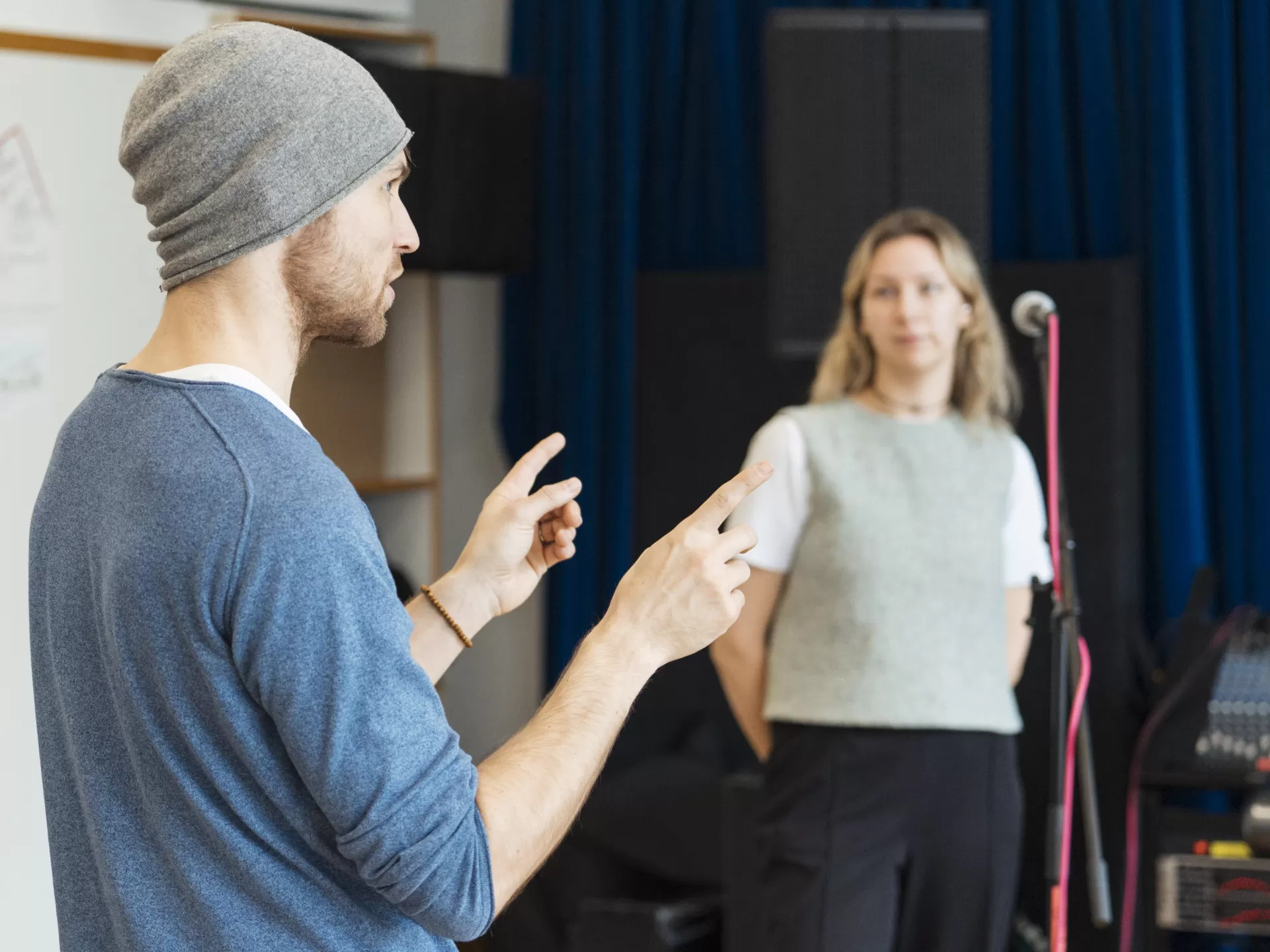 Der Coach Martin Bosch erklärt etwas und gestikuliert dabei mit seinen Armen. Im Hintergrund steht die Sängerin von Groovedivision und hört konzentriert zu.