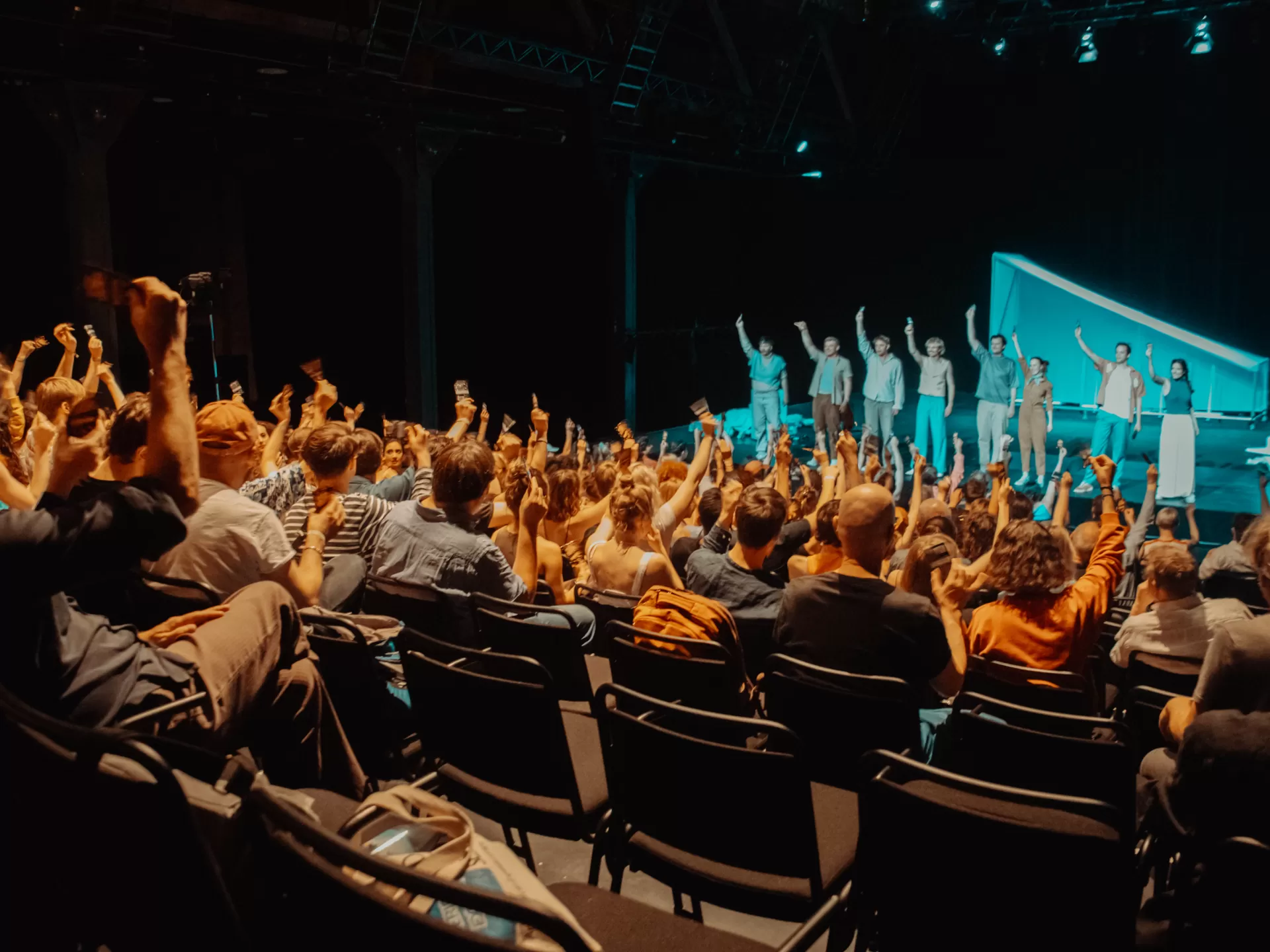 Publikum im Bockenheimer Depot, Blick auf die Bühne wo eine Gruppe Darsteller*innen das Publikum zum Mitmachen motiviert.