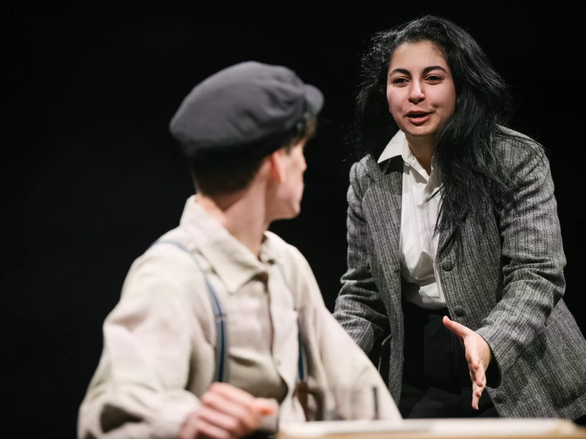 Frau in grauem Anzug spricht mit einem Mann an einem Tisch.