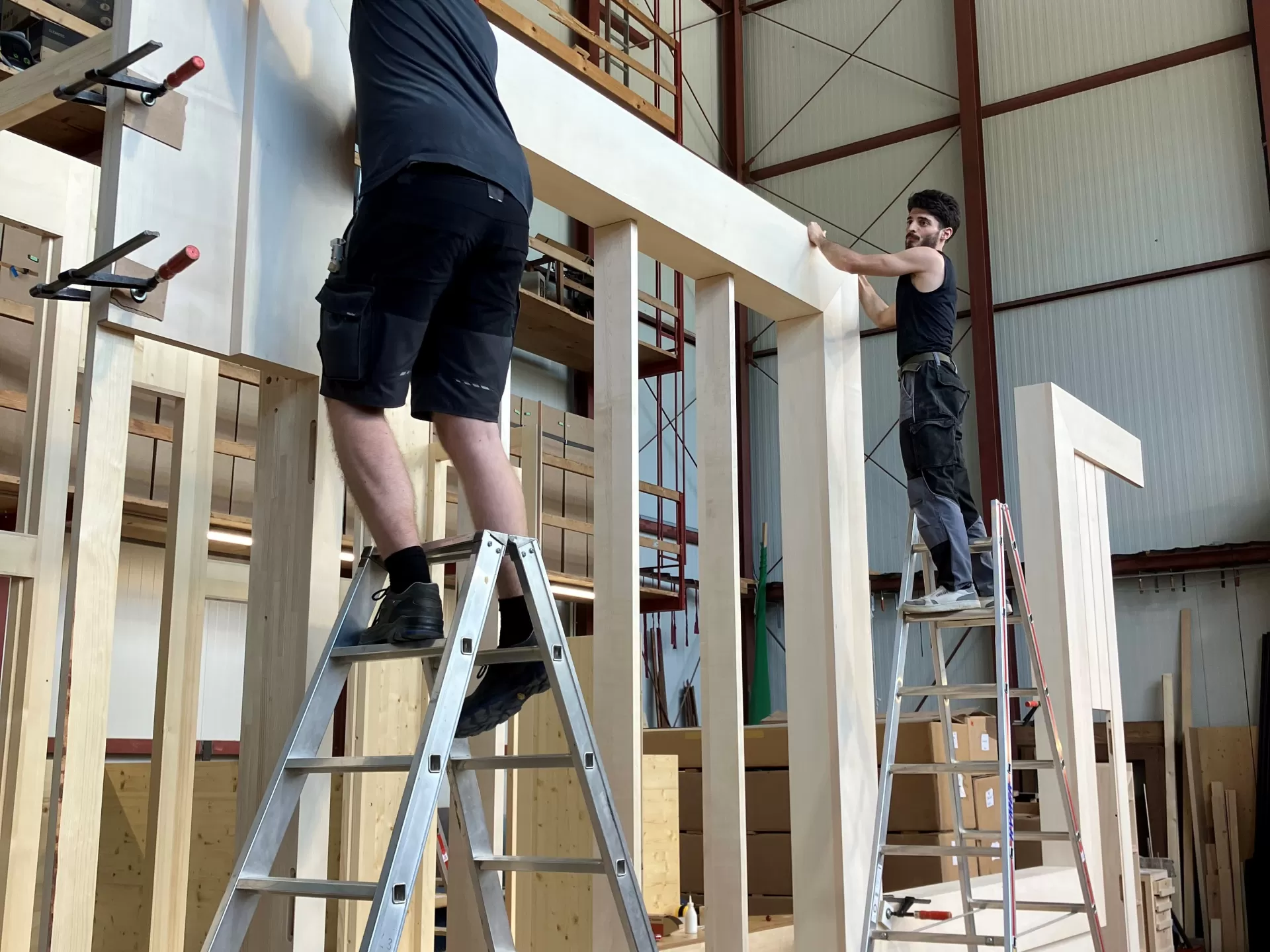 Zwei Männer stehen auf Leitern und arbeiten an einem großen Holzgehäuse.