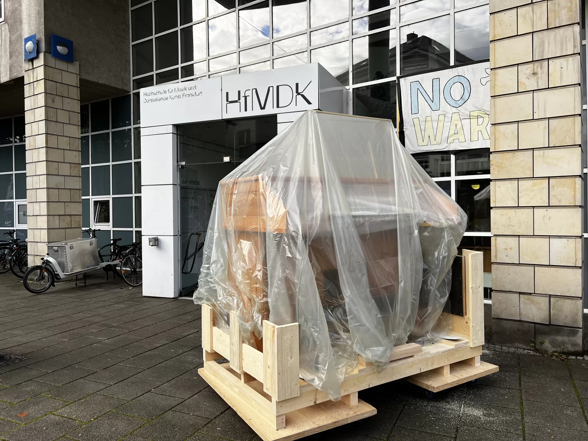 Der Spieltisch steht, unter einer Plane verpackt, vor dem Haupteingang der HfMDK.