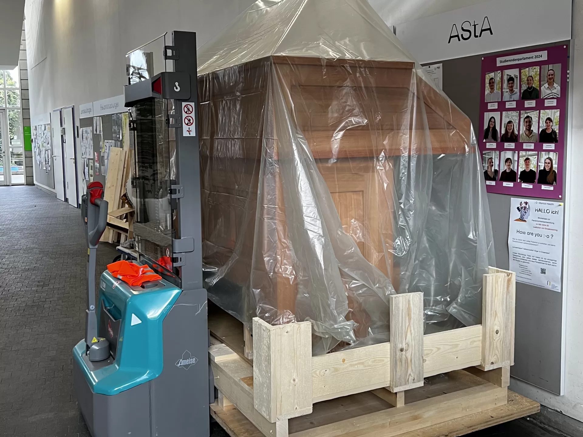 Der eingepackte Spieltisch steht vorm Schwarzen Brett im Foyer der Hochschule.