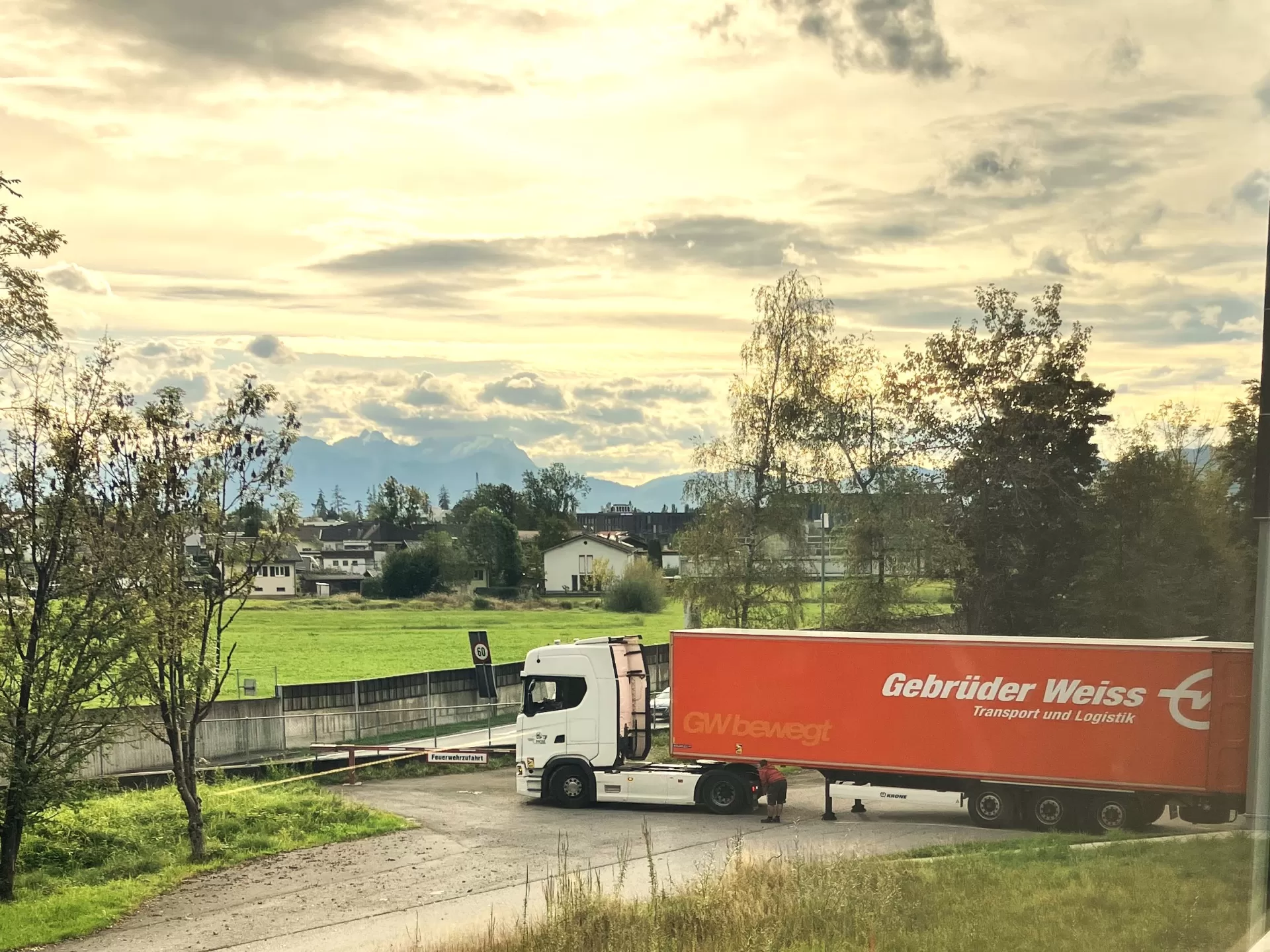 Der Lastwagen steht vor der Werkstatt. Dahinter sieht man den Ort und Berge in der Ferne.