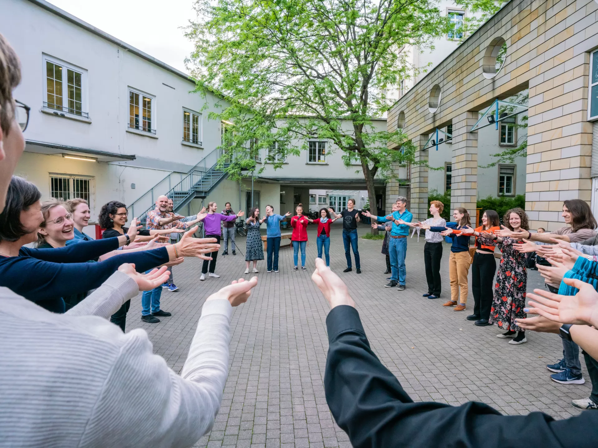 Im Innenhof stehen Menschen in einem Kreis und strecken die Hände aus in die Richtung Mitte.