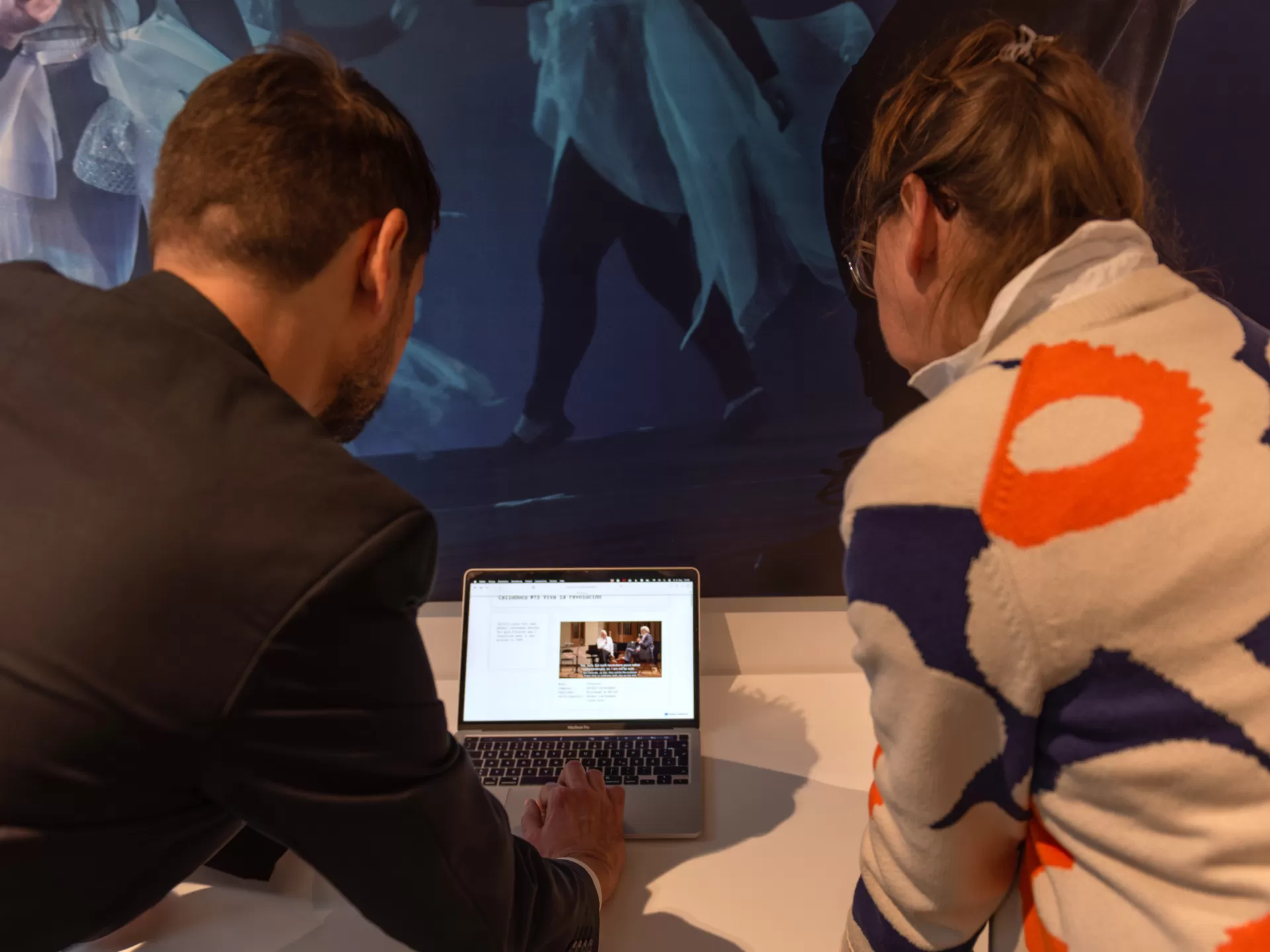 Zwei Personen von hinten, sie stehen links und rechts an einem Tisch und beugen sich nach vorn, um gemeinsam eine Präsentation anzusehen.