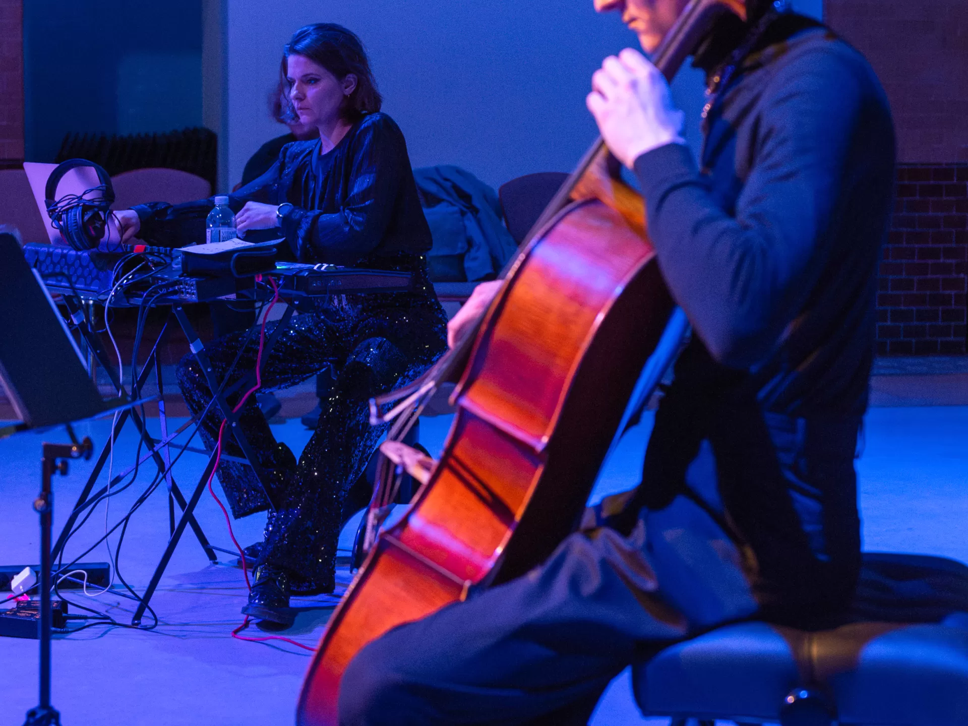 Ein Cellist spielt, im Hintergrund sitzt eine Studentin an der Elektronik. Beide sind umgeben von blauem Licht.
