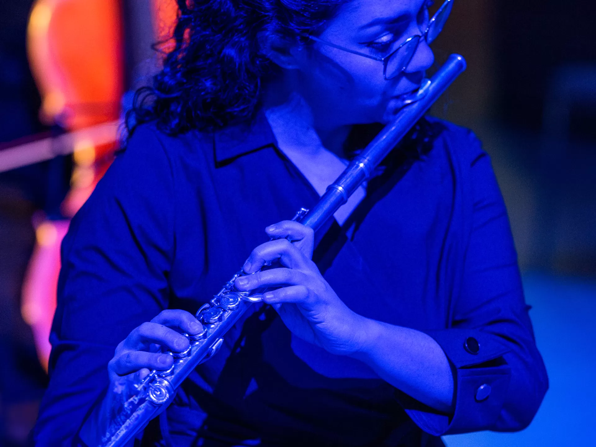 Eine Flötistin spielt auf ihrer Querflöte, umgeben von blauem Licht.