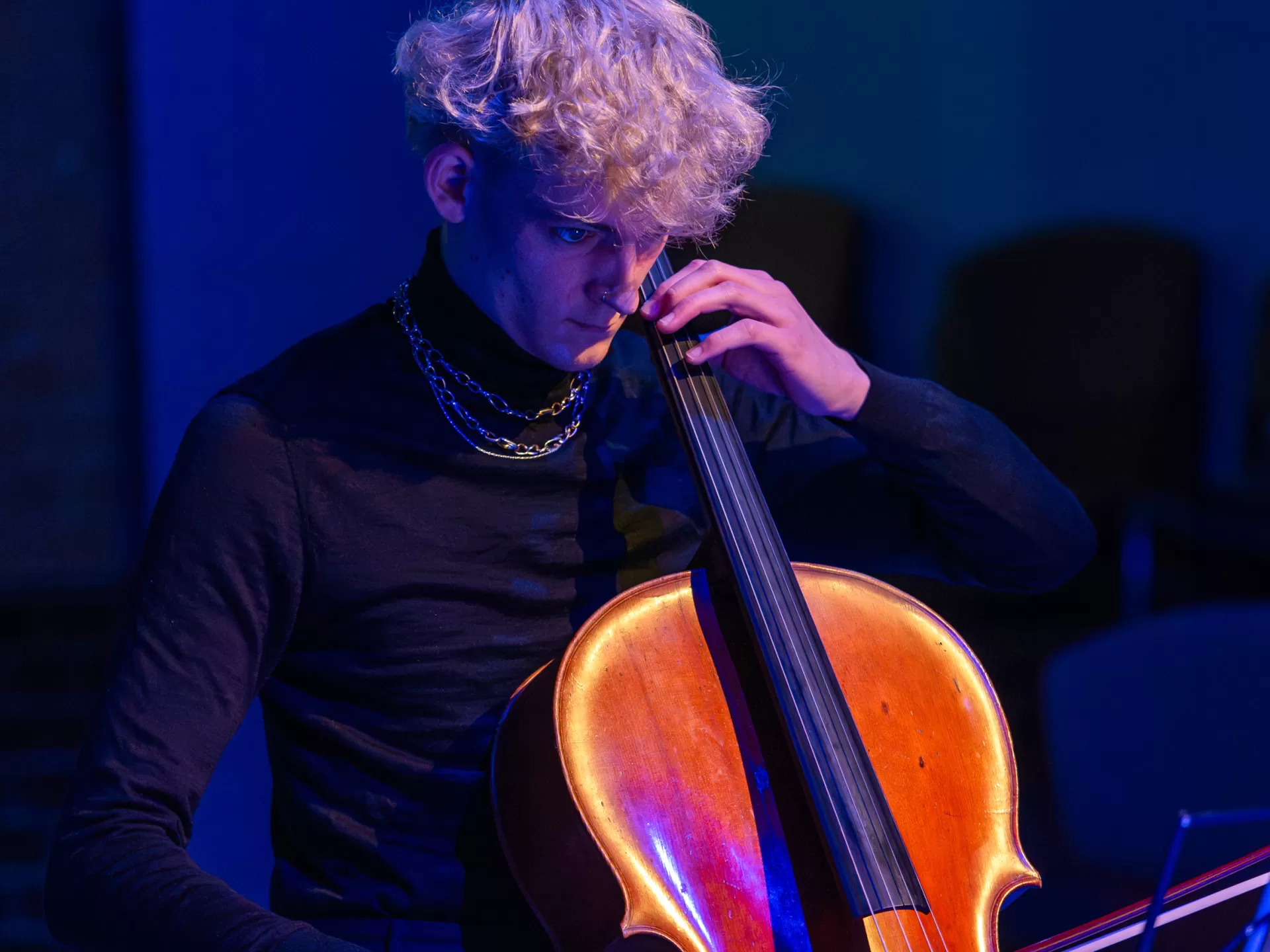 Ein Student spielt Cello. Um ihn herum ist blaues Licht.