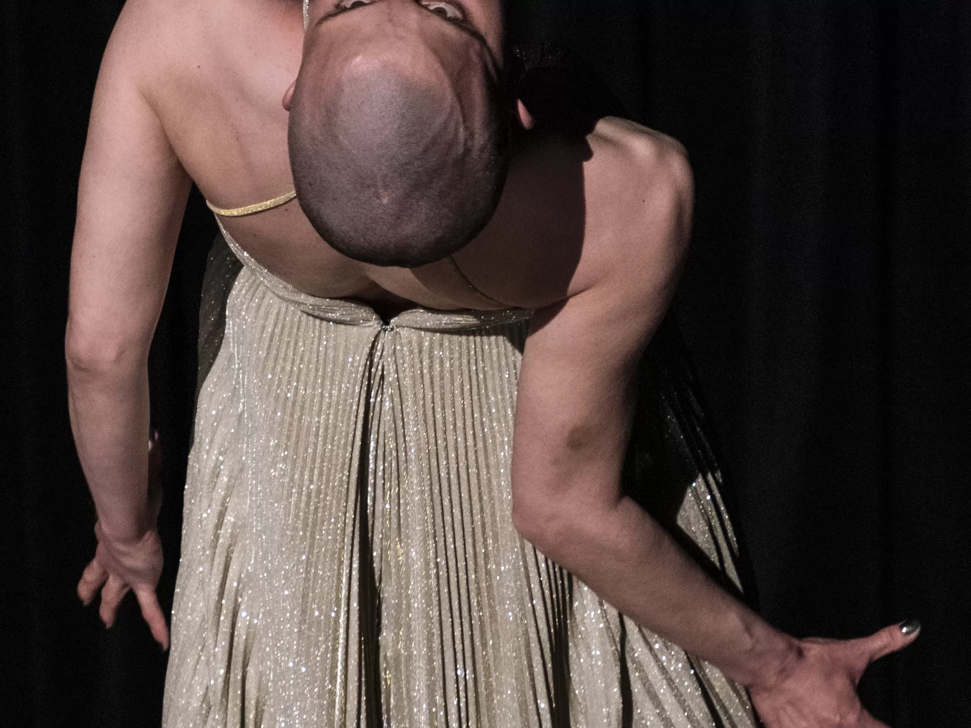 Lisa steht mit dem Rücken zum Publikum und beugt sich angespannt nach hinten. Sie trägt ein silbernes, glitzerndes Kleid.