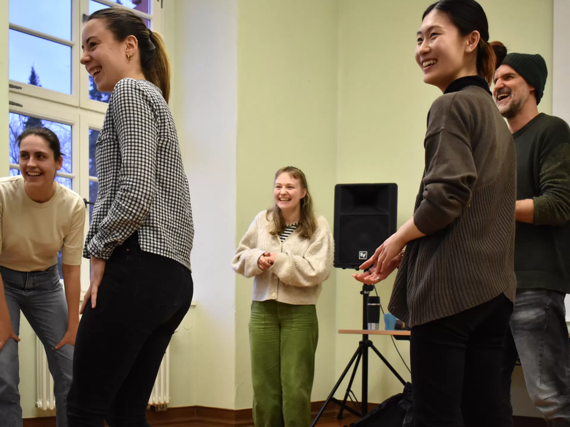 Eine Gruppe von Studierenden und ein Dozierender stehen im Kreis, sie wenden sich an eine Person außerhalb des Bildes und lächeln.