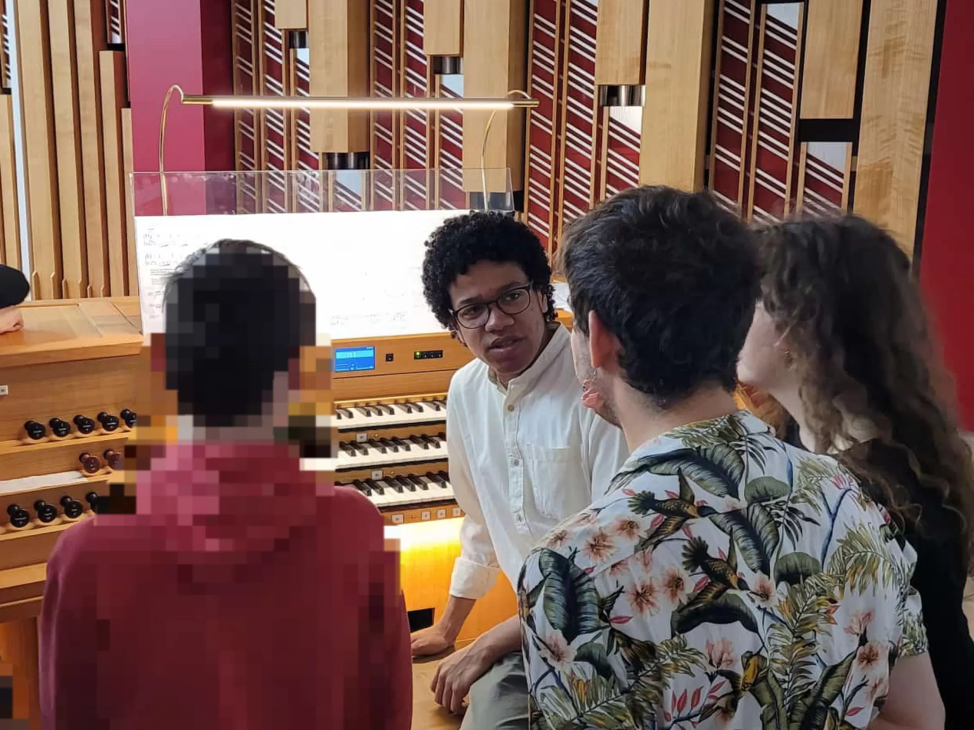 Ein Student sitzt auf der Orgelbank, zwei weitere Studierende stehen daneben und unterhalten sich mit einem Schüler