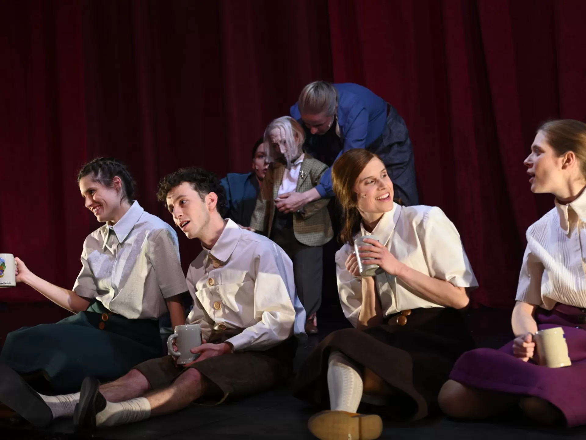 Lisa Feiberger sitzt als Vroni in einer Gruppe, hält einen Bierkrug und spricht mit einer Freundin.