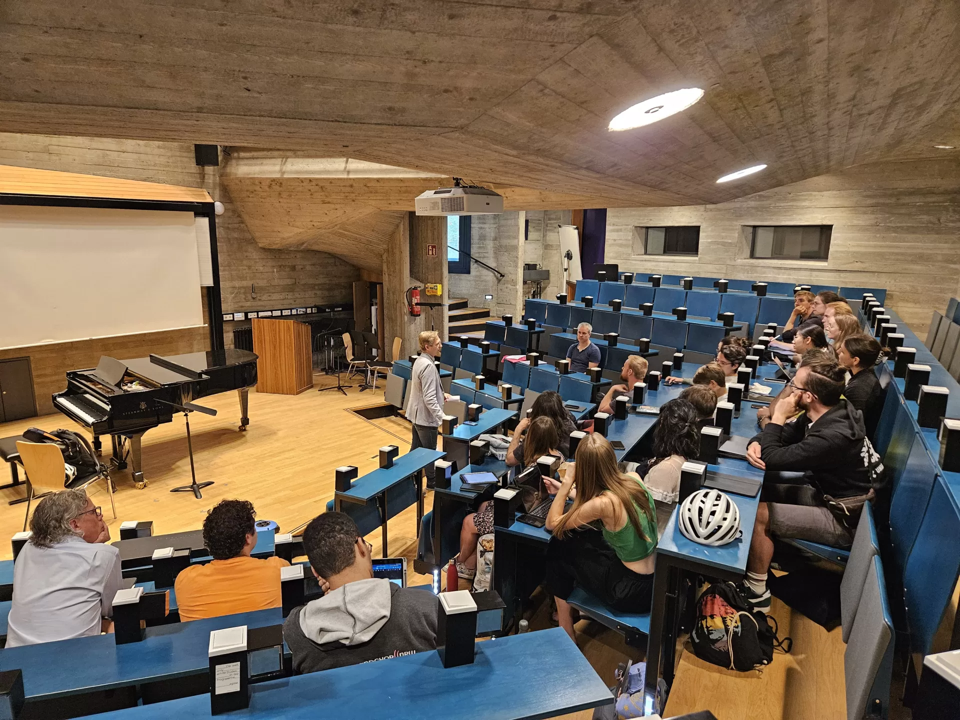 Im Hörsaal. Florian Lohmann steht vorne und erzählt, die Studierende sitzen in den Reihen und hören zu.