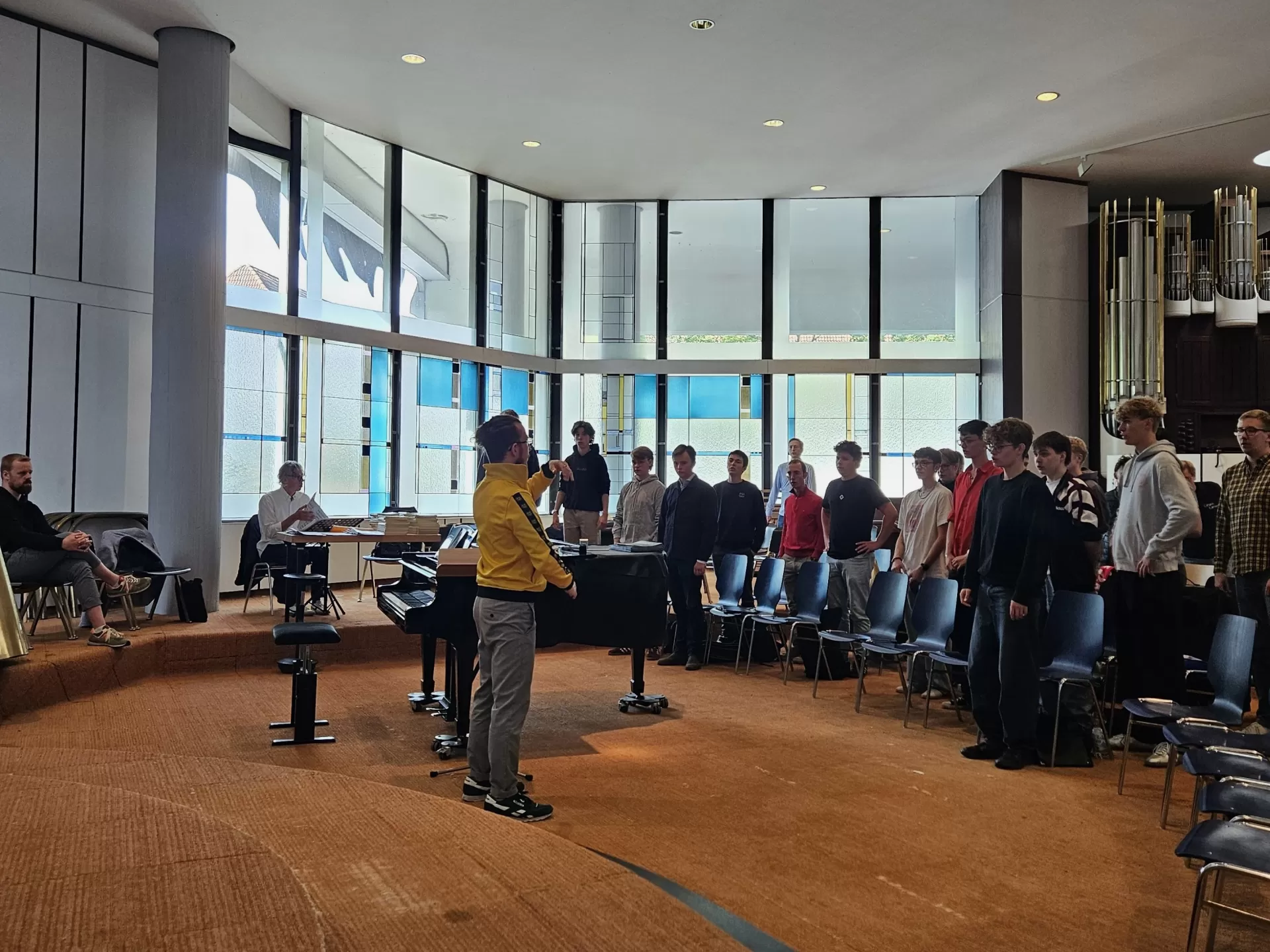 Probe mit den Männerstimmen des Knabenchores in ihrem Probenraum, einer Kirche. Student steht vorne und leitet gestisch das Einsingen an.