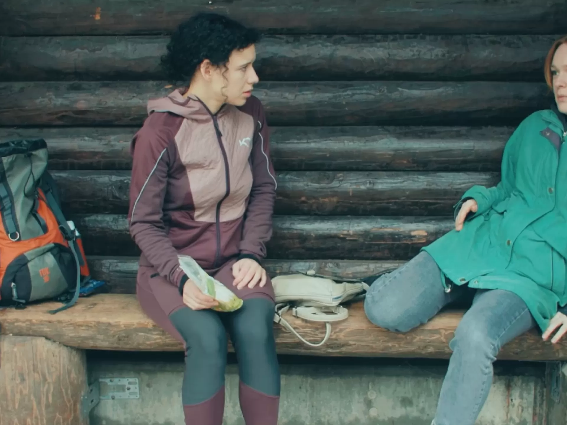 Zwei Frauen an einer Bushaltestelle in Wanderbekleidung.