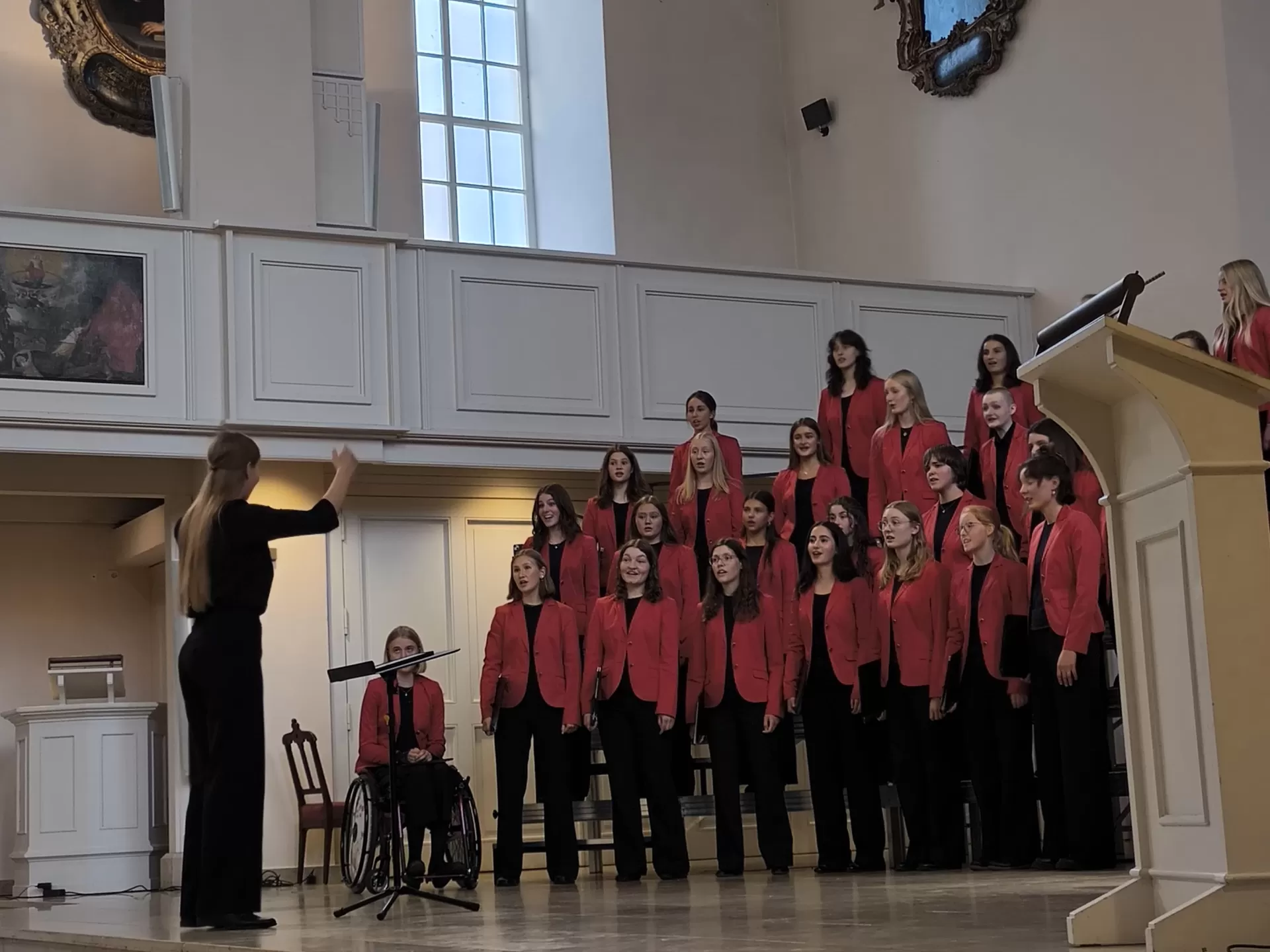 Abschlusskonzert. Mädchenchor singt im Altarraum, Studentin dirigiert.