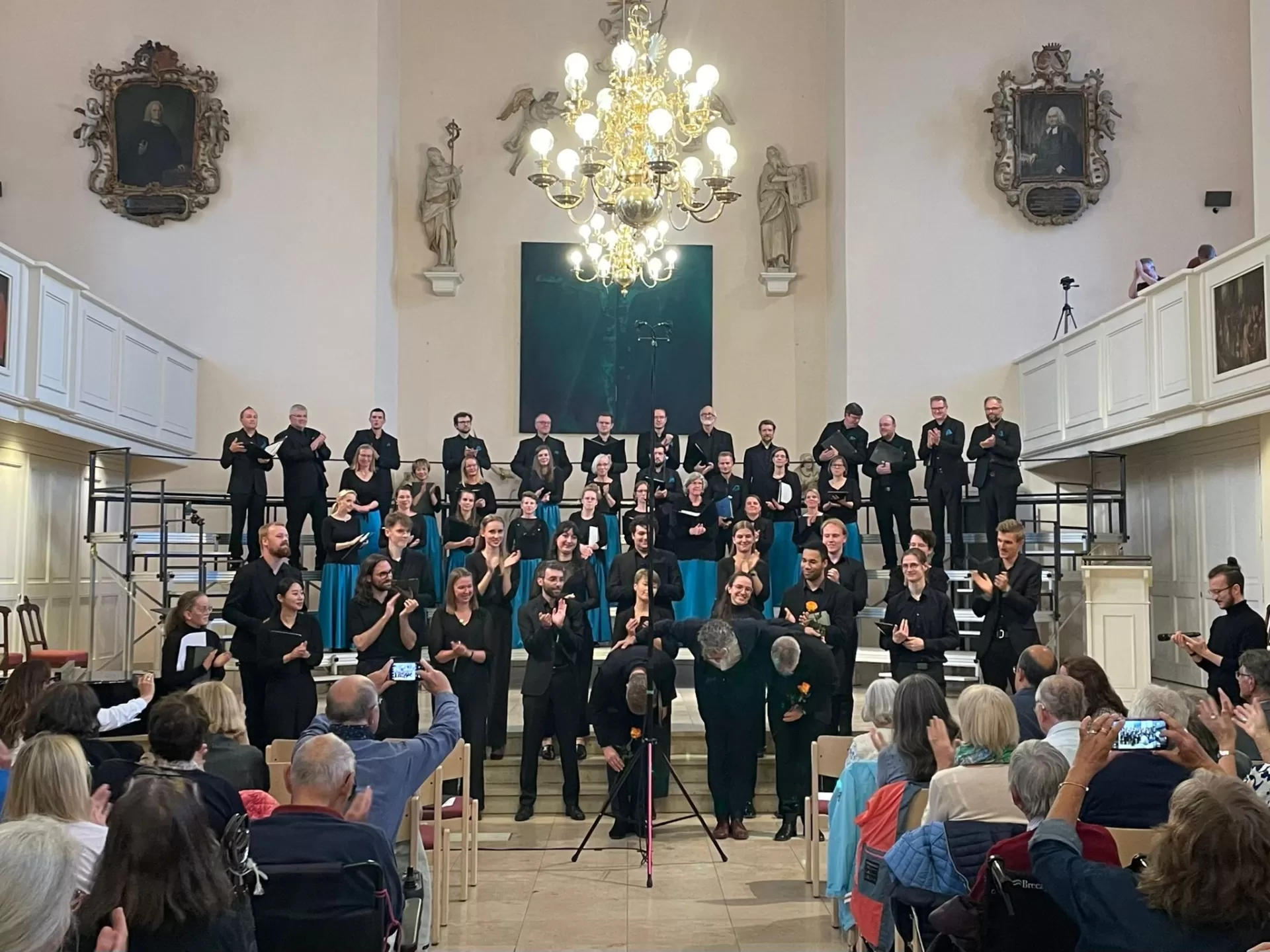 Abschlusskonzert. Blick auf Altarraum/Bühne mit Collegium Vocale im Hintergrund, davor teilnehmende Studierende und die drei Professoren, die sich verbeugen.