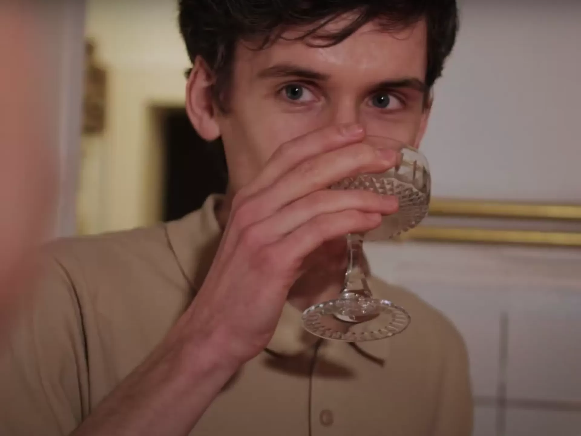 Ein Mann trinkt in einer Küche aus einem Cocktailglas.