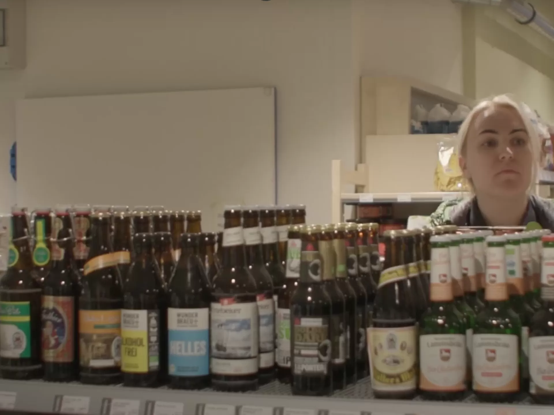 Eine Mitarbeiterin schaut in einem Supermarkt prüfend über ein Regal hinweg.